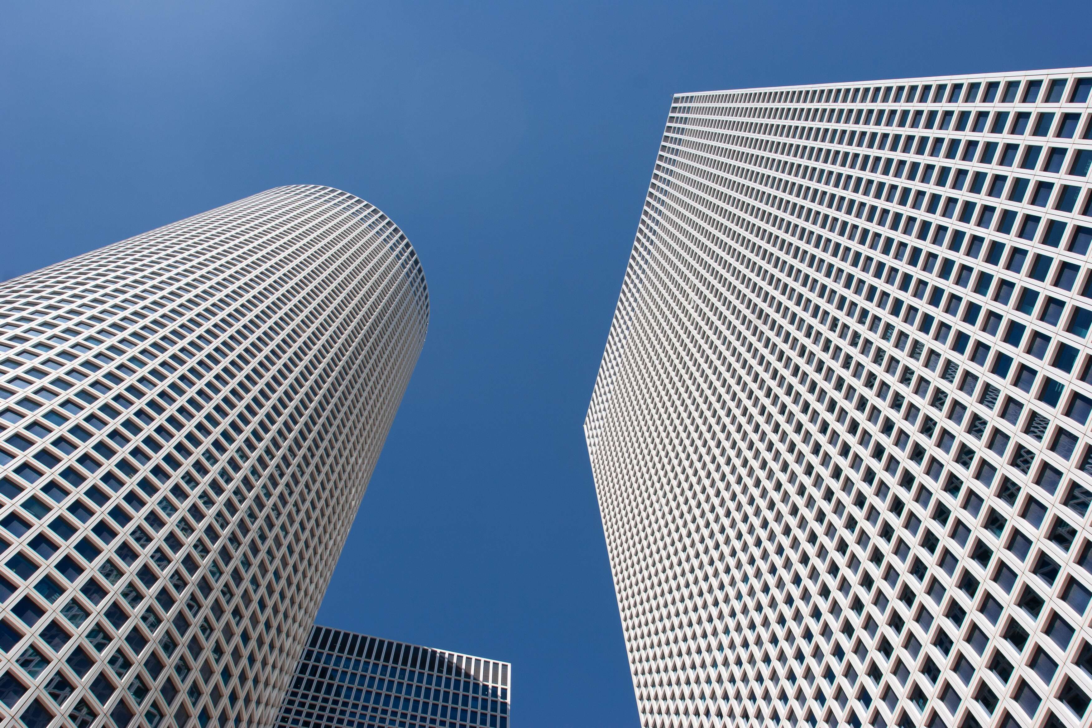 The Azrieli Towers stretch into the cloudless sky, their sleek, geometric facades creating a striking image of modern architectural elegance. The photograph captures the harmony of curves and straight lines, symbolizing the balance between innovation and design in urban spaces. Tel Aviv, Israel