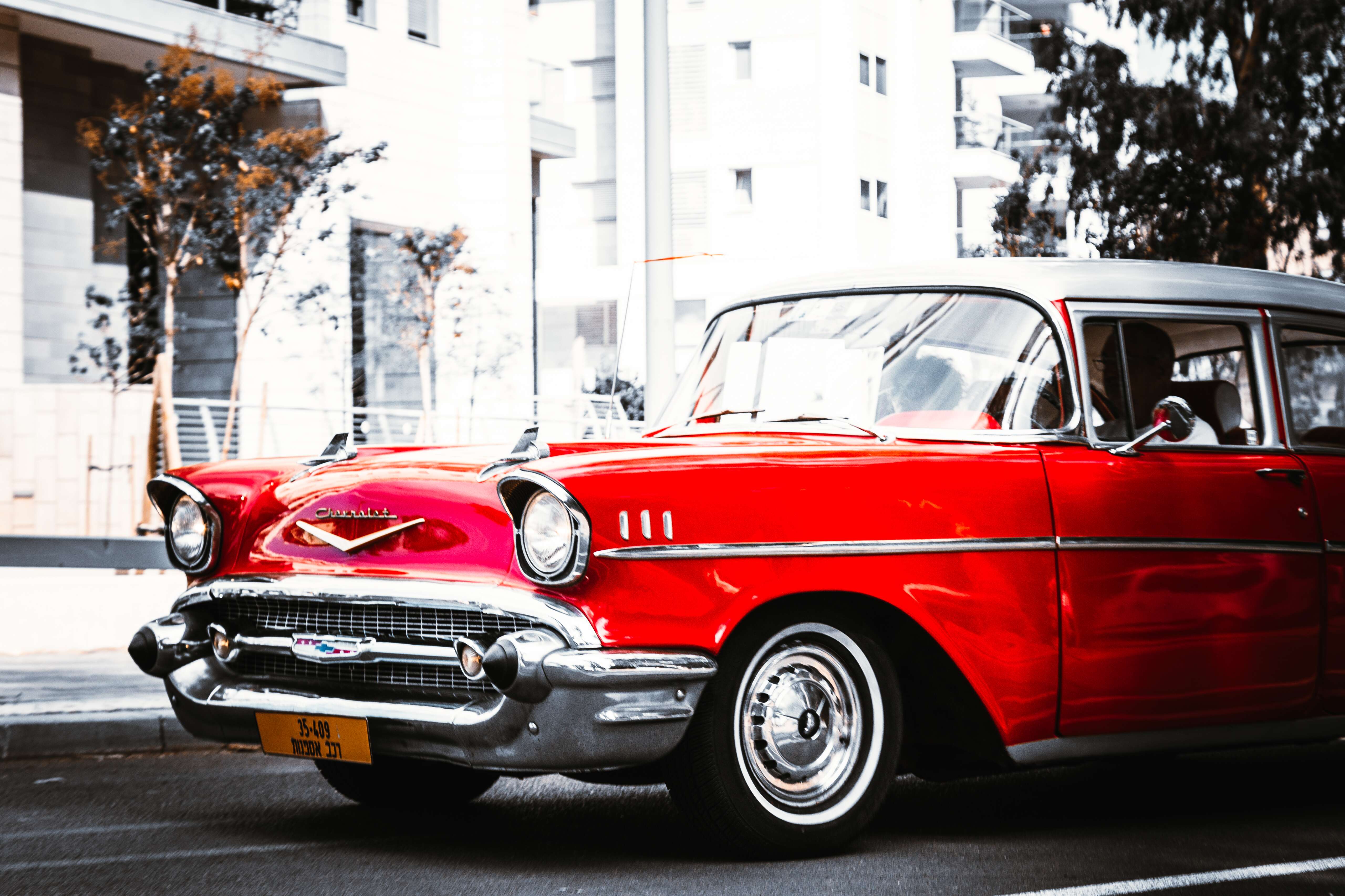 A striking red vintage Chevrolet with chrome details parked near modern buildings, part of a retro car event. Retro Car Club Leumi, Tel Aviv, Israel