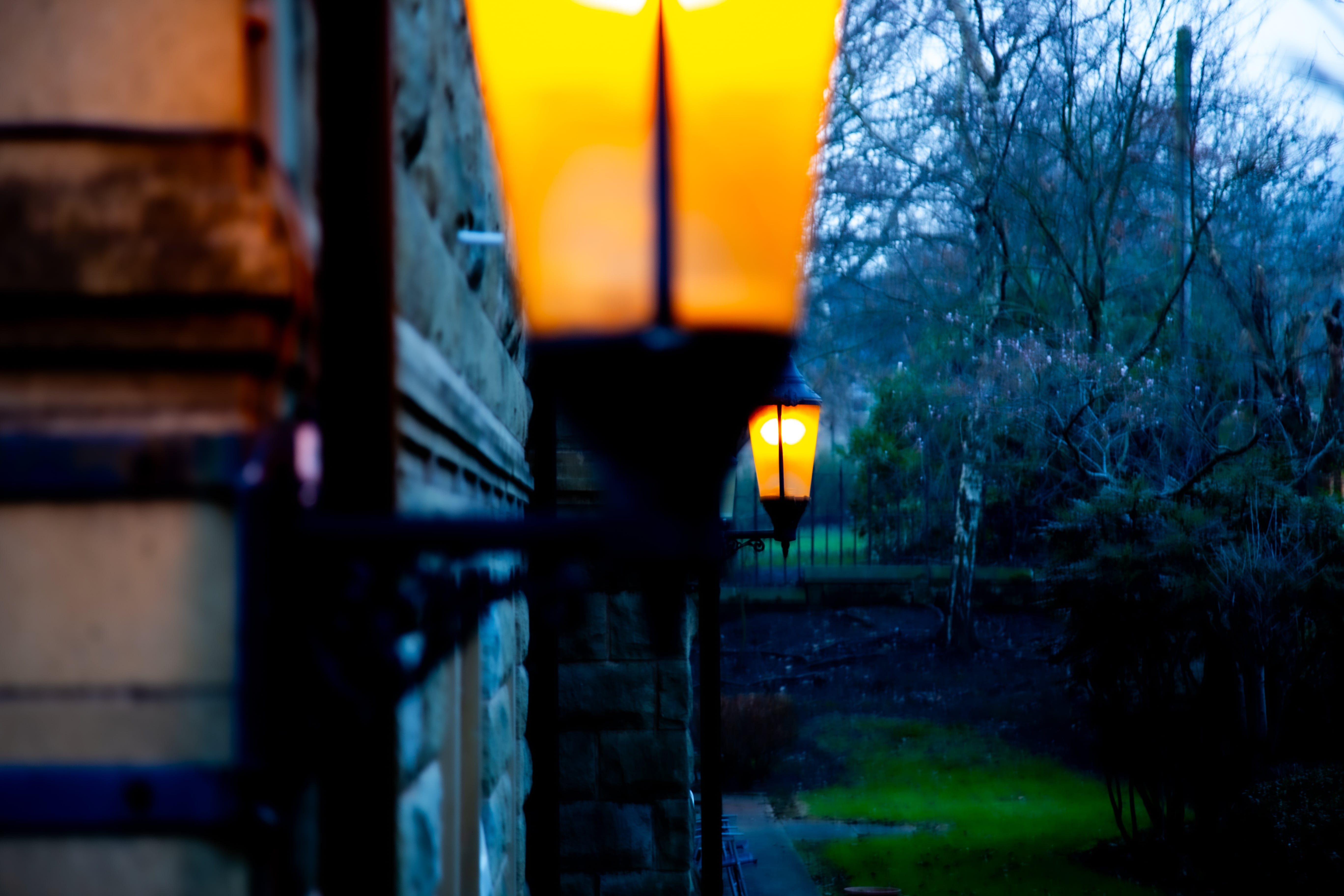 Softly glowing street lamps cast light over cool evening blues, creating a nostalgic atmosphere against old stone architecture in Halifax. Halifax, God’s Own Country (Yorkshire), Great Britain