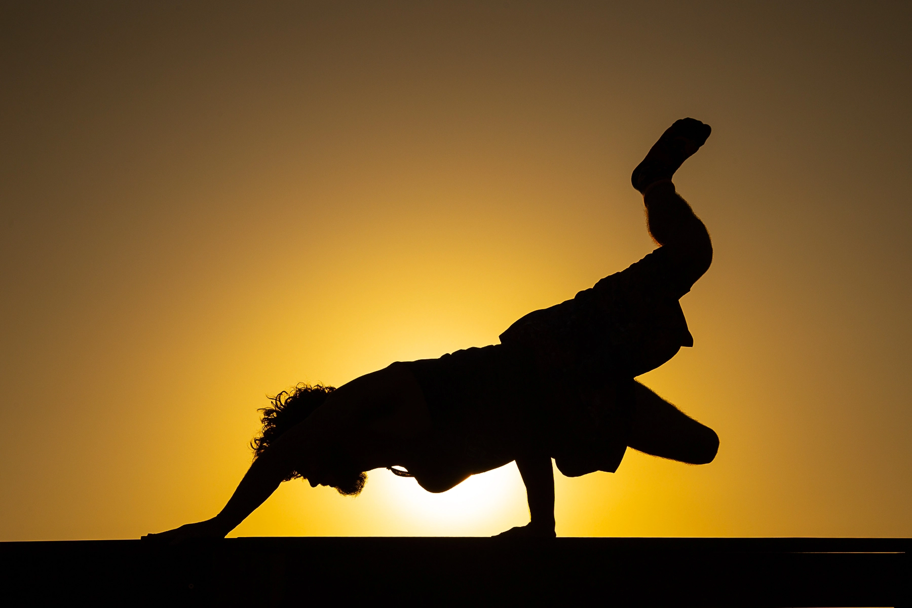 Silhouette of a person performing a handstand-like pose against a vivid sunset backdrop. Mitzpe Ramon, Israel