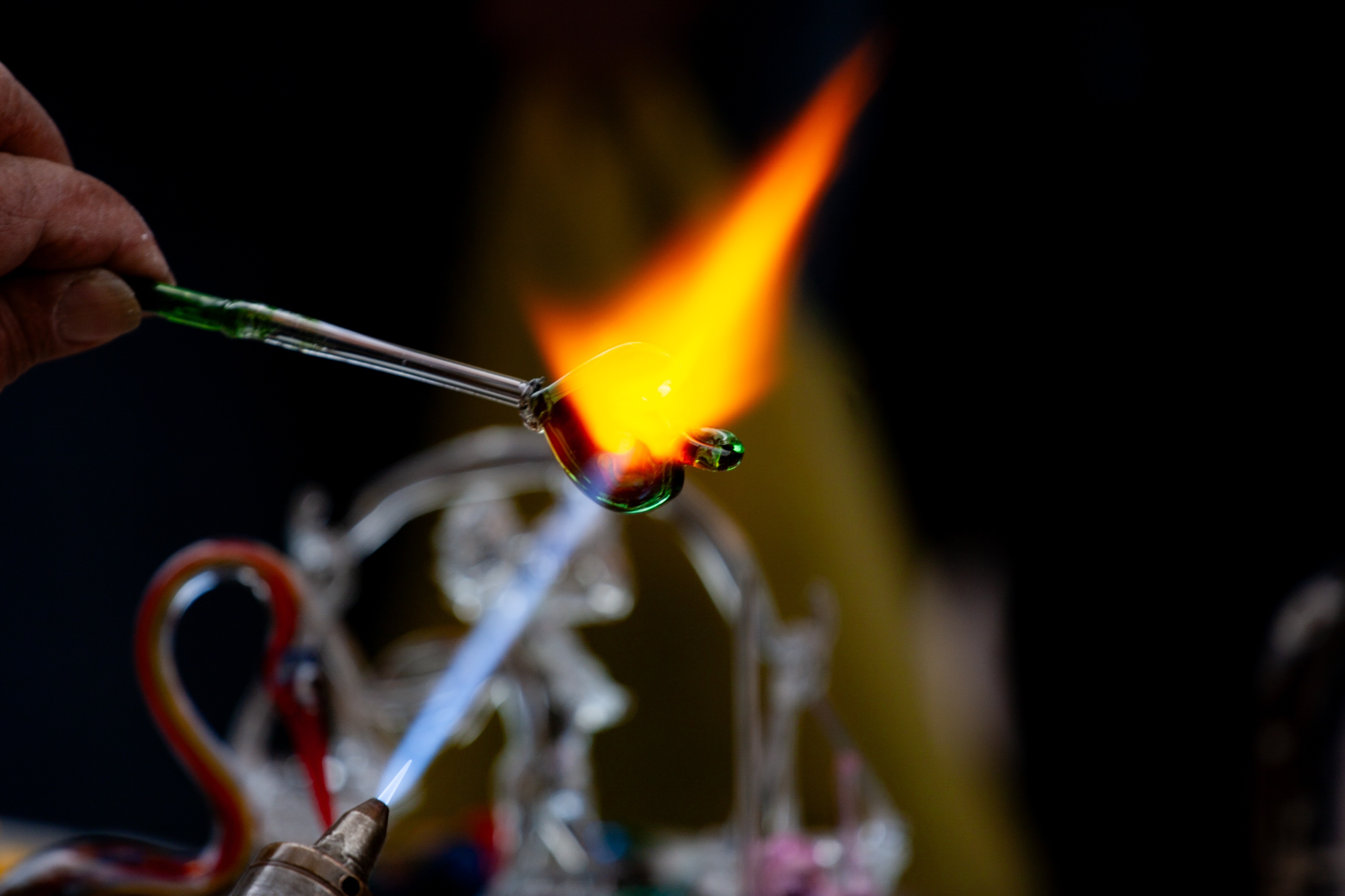 An artisan carefully forms a glass heart over an open flame, demonstrating the delicate process of glassblowing. Tel Aviv, Israel