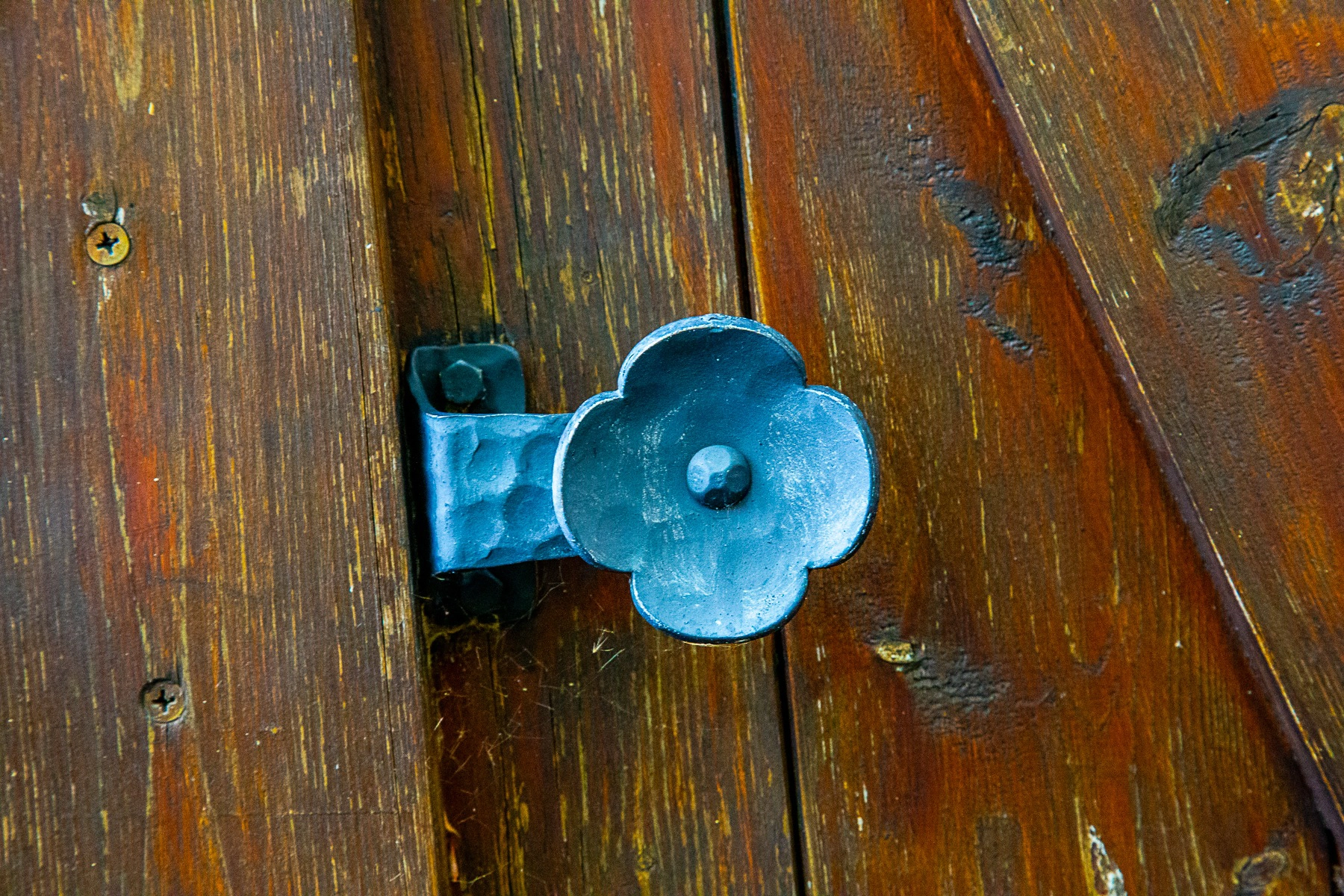 A metal door handle shaped like a flower, mounted on a weathered wooden door. Dürnstein, Austria