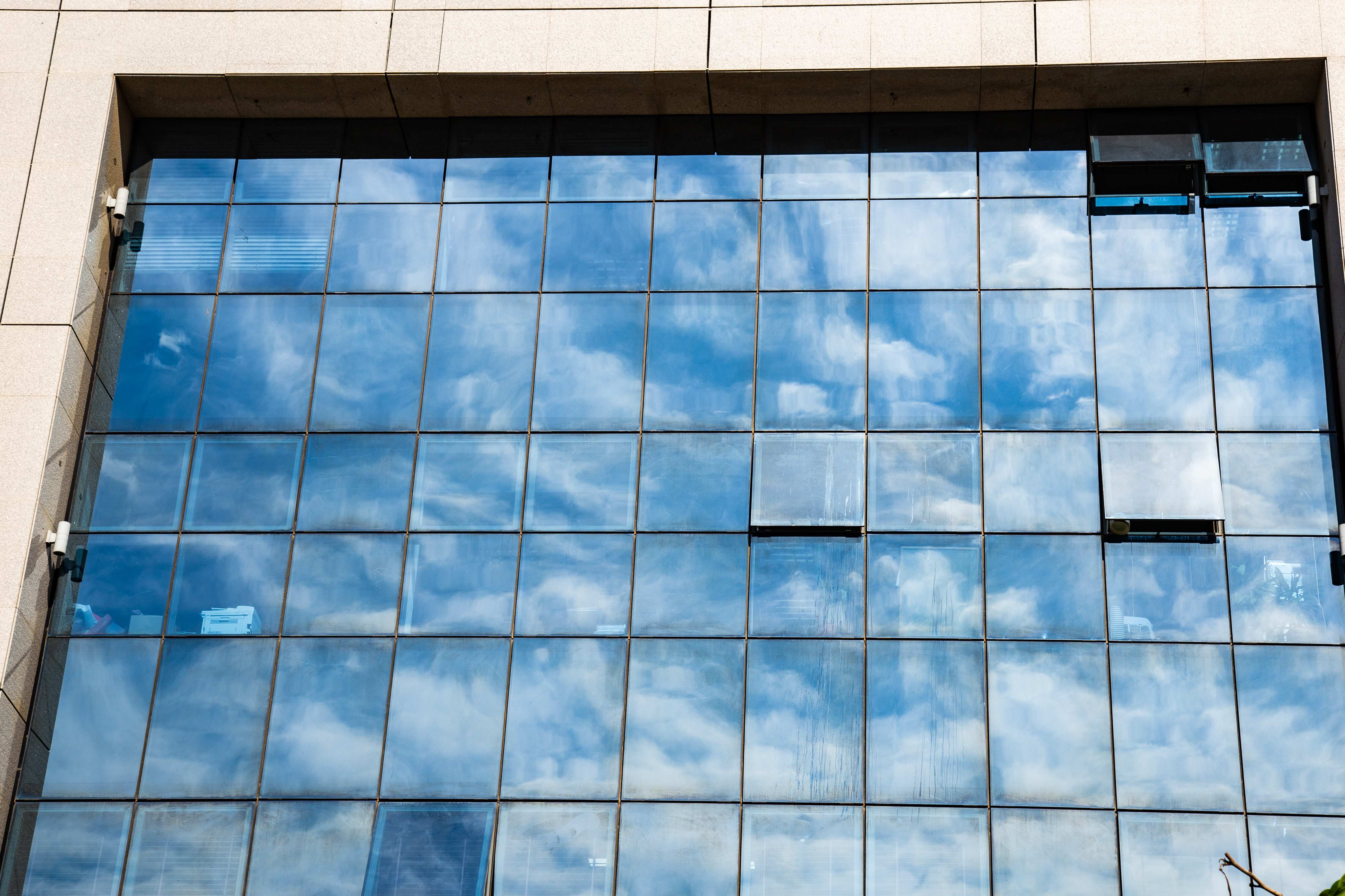 A glass building reflecting a vivid blue sky with scattered clouds, creating a mirrored effect. Tel Aviv, Israel