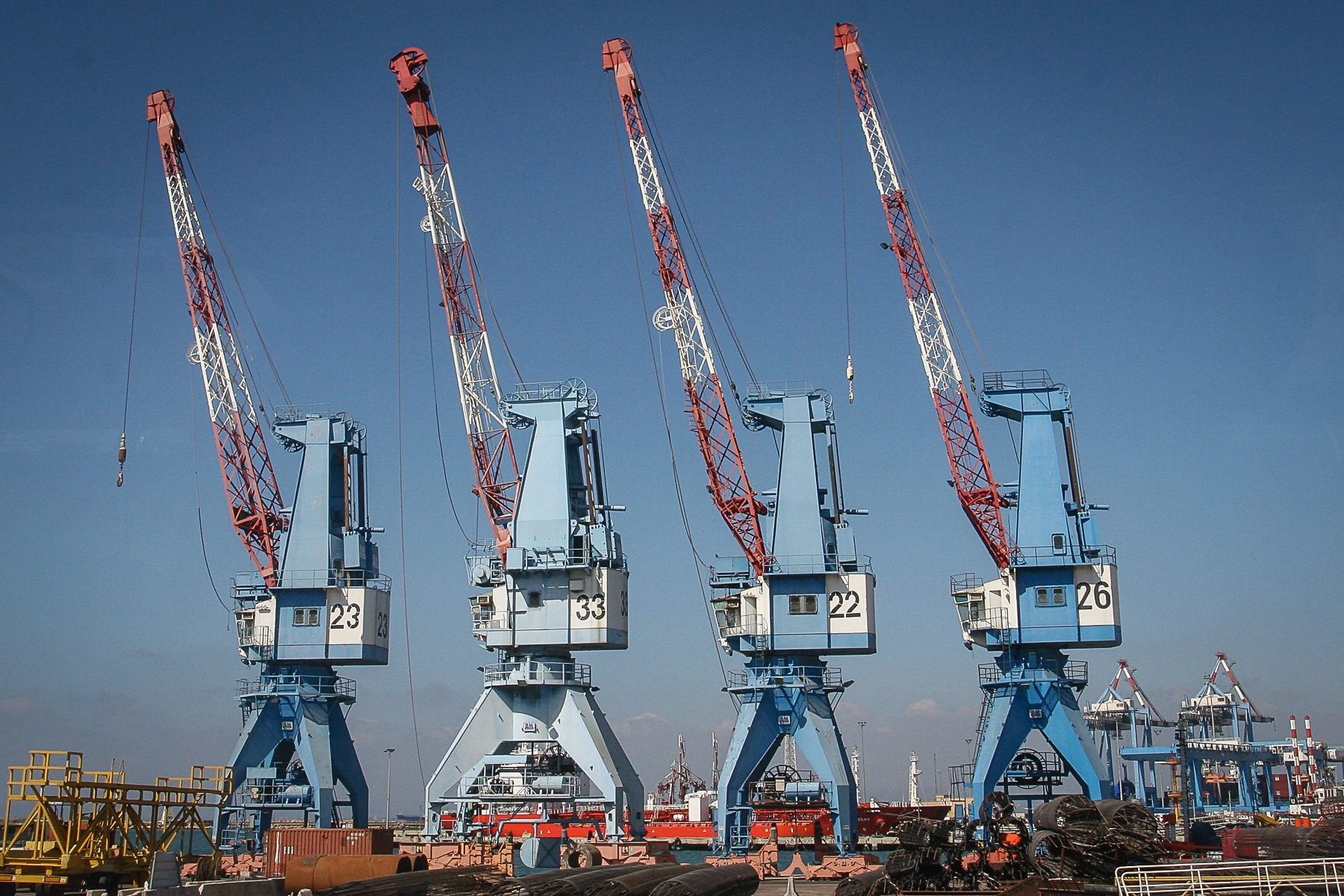 Four large, blue and red cranes standing in Haifa's port, used for industrial shipping purposes against a clear blue sky. Haifa, Israel