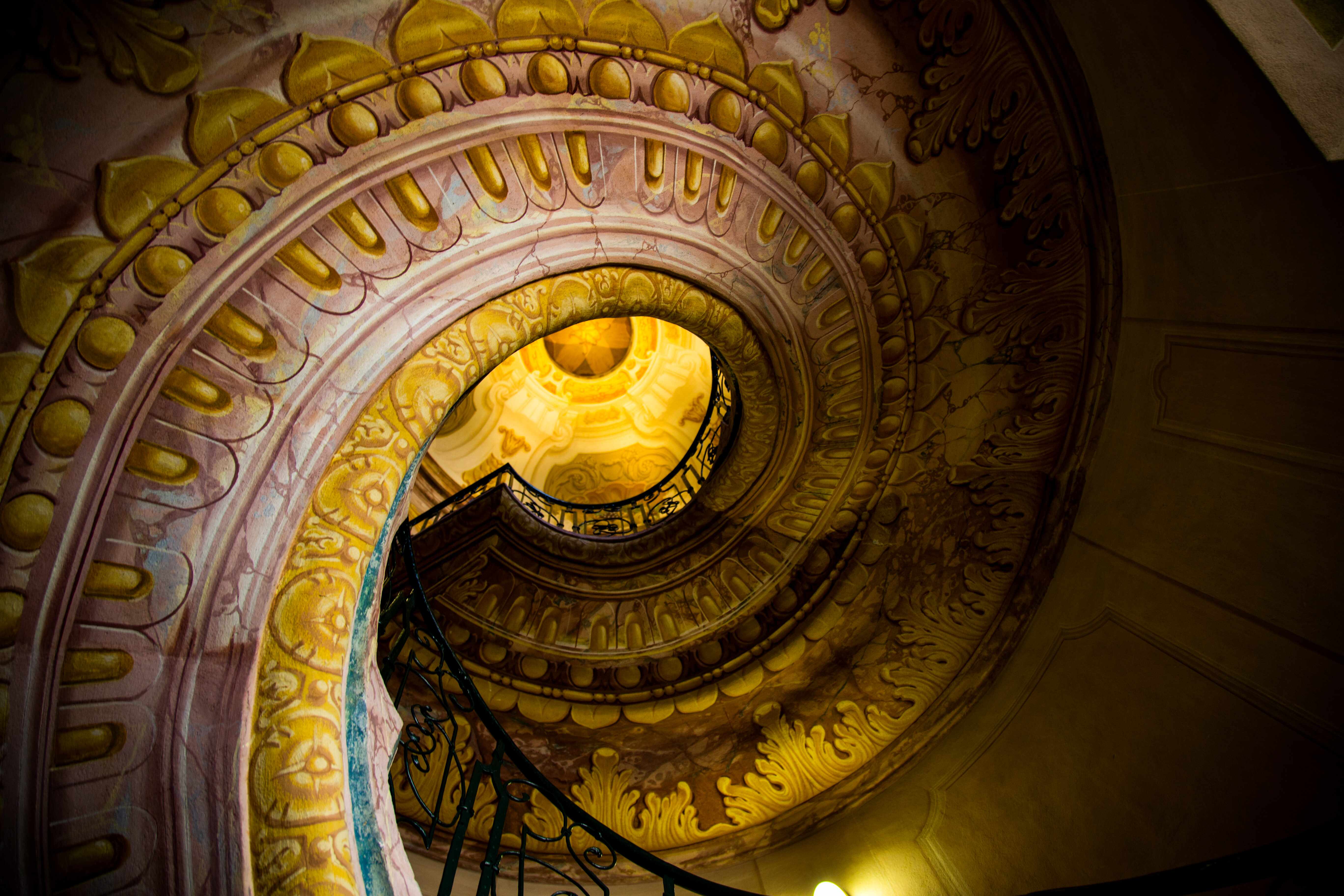 A stunning spiral staircase with ornate golden and pink designs, leading upward towards a domed ceiling. Melk, Austria