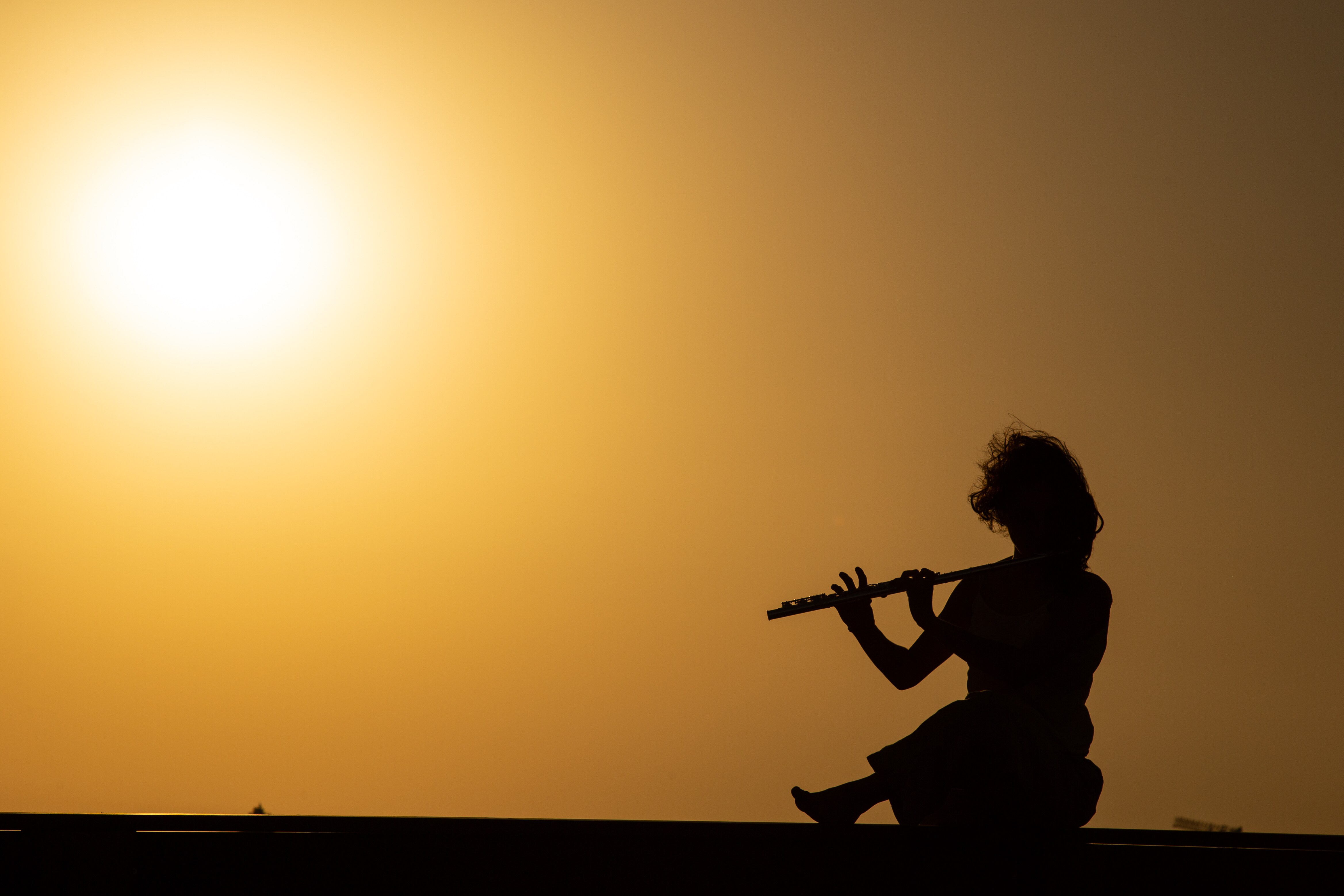 Silhouette of a flutist playing against a golden sunset, seated in a peaceful pose. Mitzpe Ramon, Israel