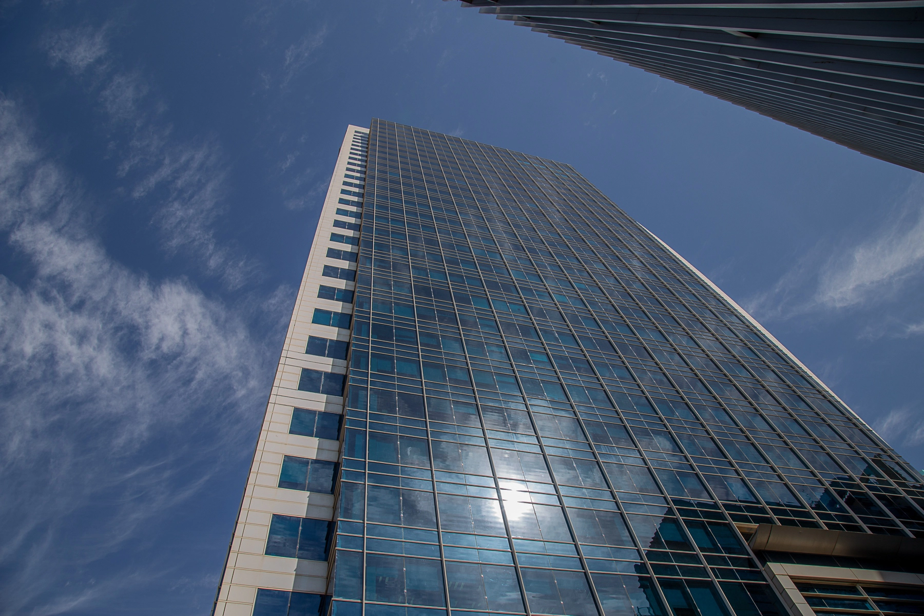 A low-angle view of a modern glass skyscraper in Tel Aviv reflecting the sun, with a vibrant blue sky and light cloud streaks. Tel Aviv, Israel