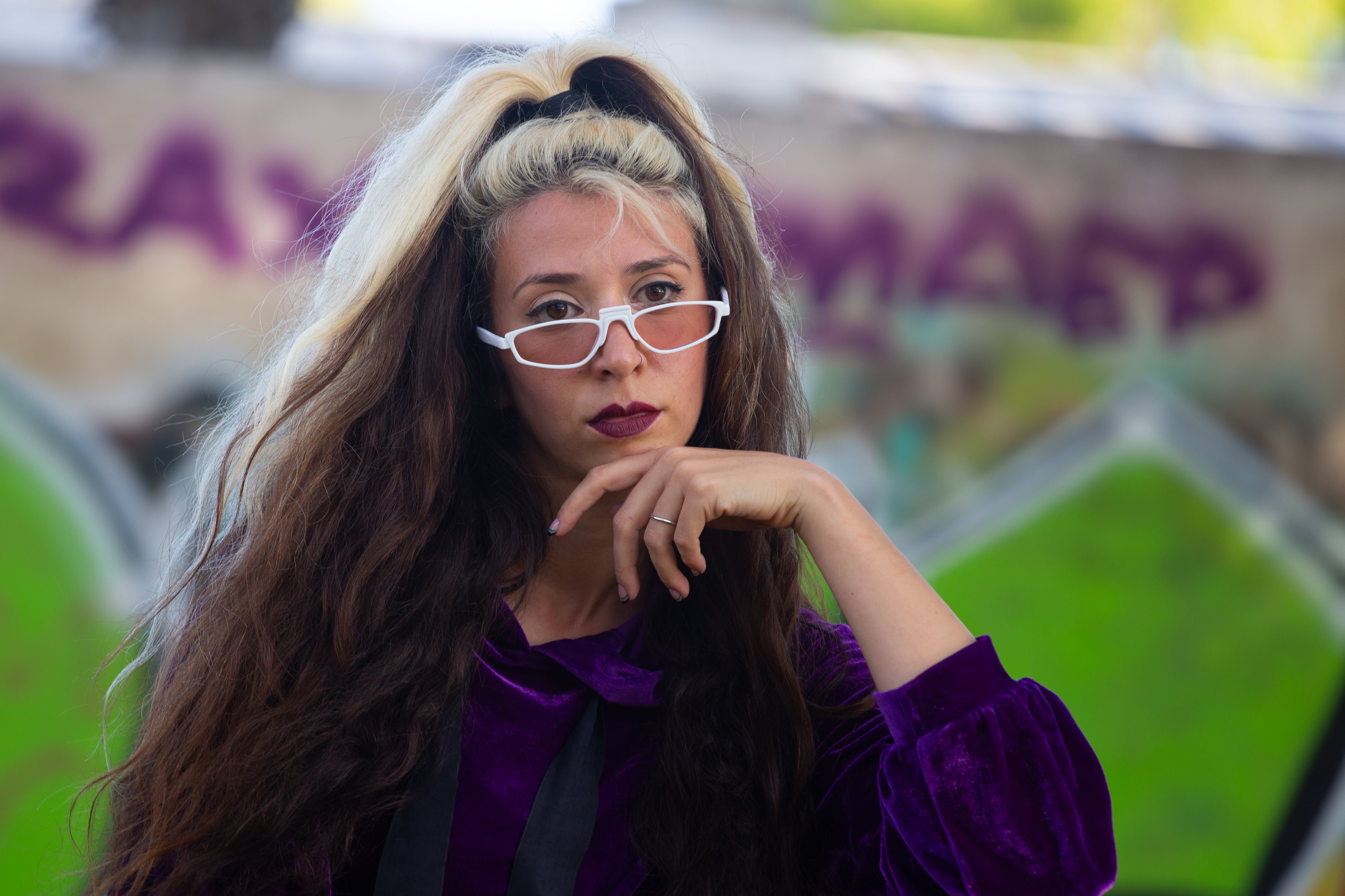 A woman with long, voluminous hair, wearing white glasses, gazes thoughtfully at the camera. Tel Aviv, Israel