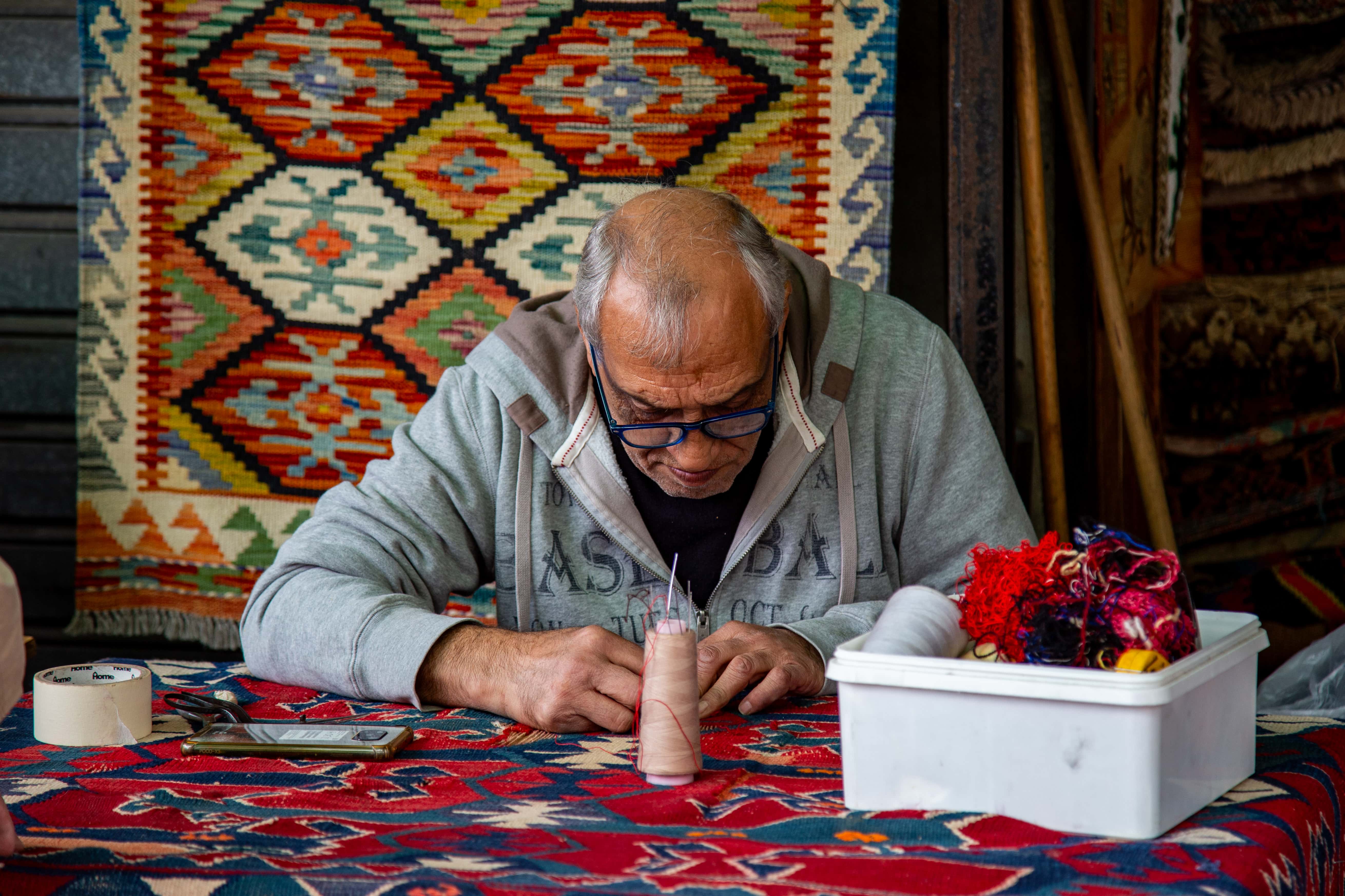 A skilled artisan works intently with threads at Jaffa Flea Market, surrounded by vibrant textiles. Tel Aviv Flea Market, Israel