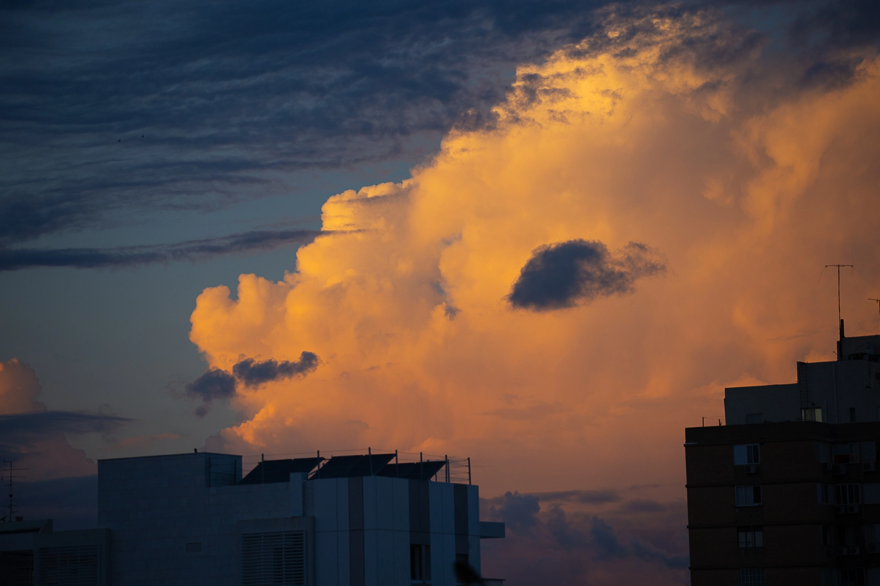 Puffy clouds lit by the sunset's golden hue, with building silhouettes in the foreground and a mix of light and dark shades in the sky. Hertzliya, Israel