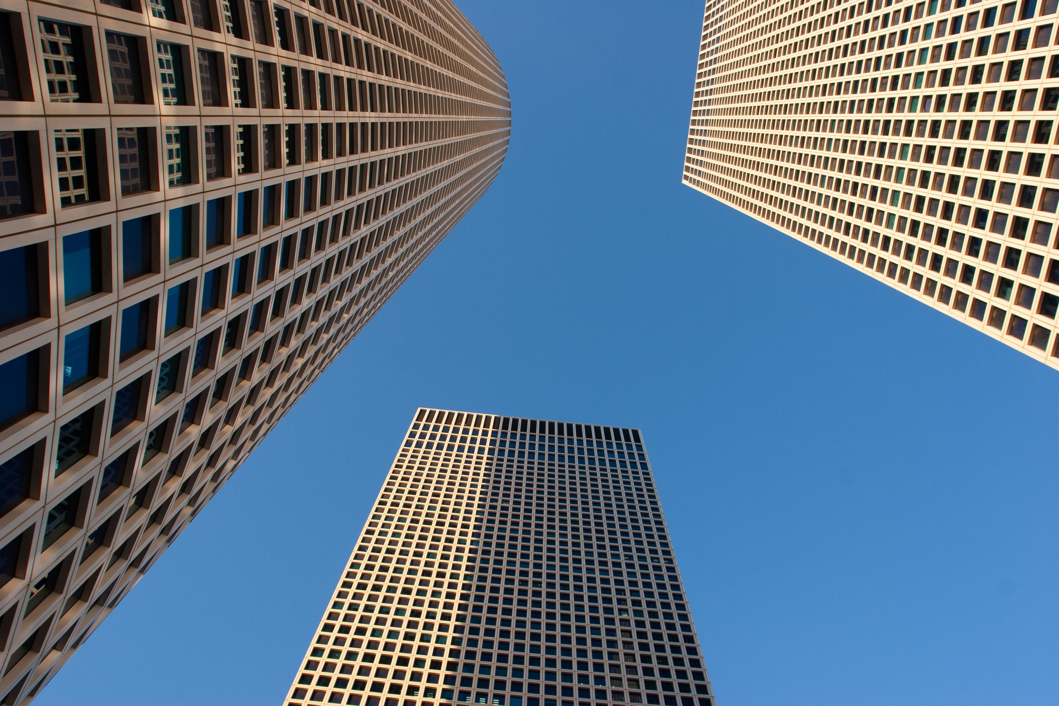 An upward perspective of the Azrieli Towers creates a mesmerizing geometric composition, where towering grids meet the vibrant blue sky. The symmetrical lines and shapes evoke a sense of order, strength, and modern architectural beauty, symbolizing humanity’s reach for the sky. Tel Aviv, Israel