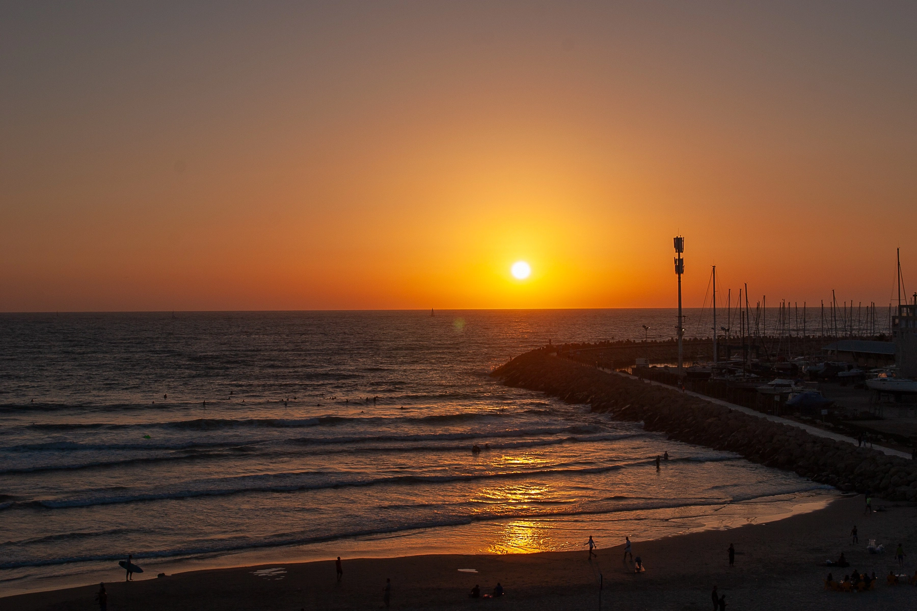 A stunning sunset over the sea, with a view of a marina and people on the beach. Hertzliya,Israel