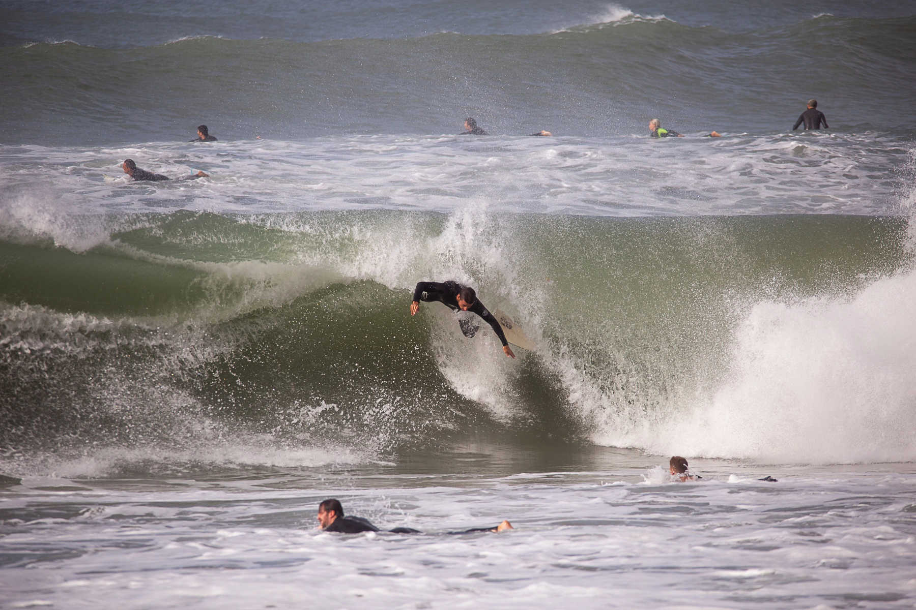 Surfers riding and navigating the waves at a marina, with some in the water and others catching waves. Marina Hertzlya, Israel