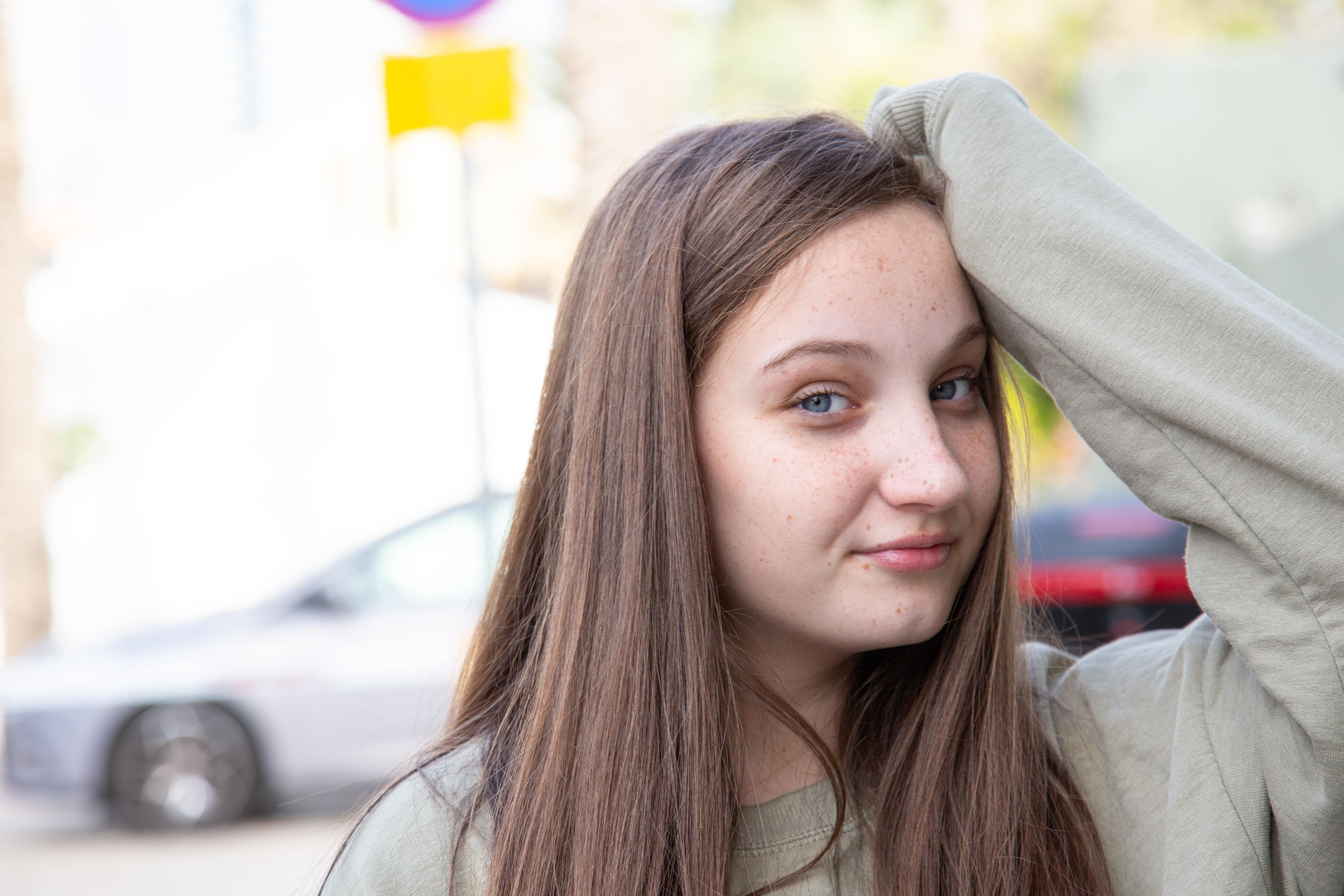 A young girl with long hair and freckles smiles slightly, posing outdoors in a relaxed manner. Neve Tzedek, Tel Aviv