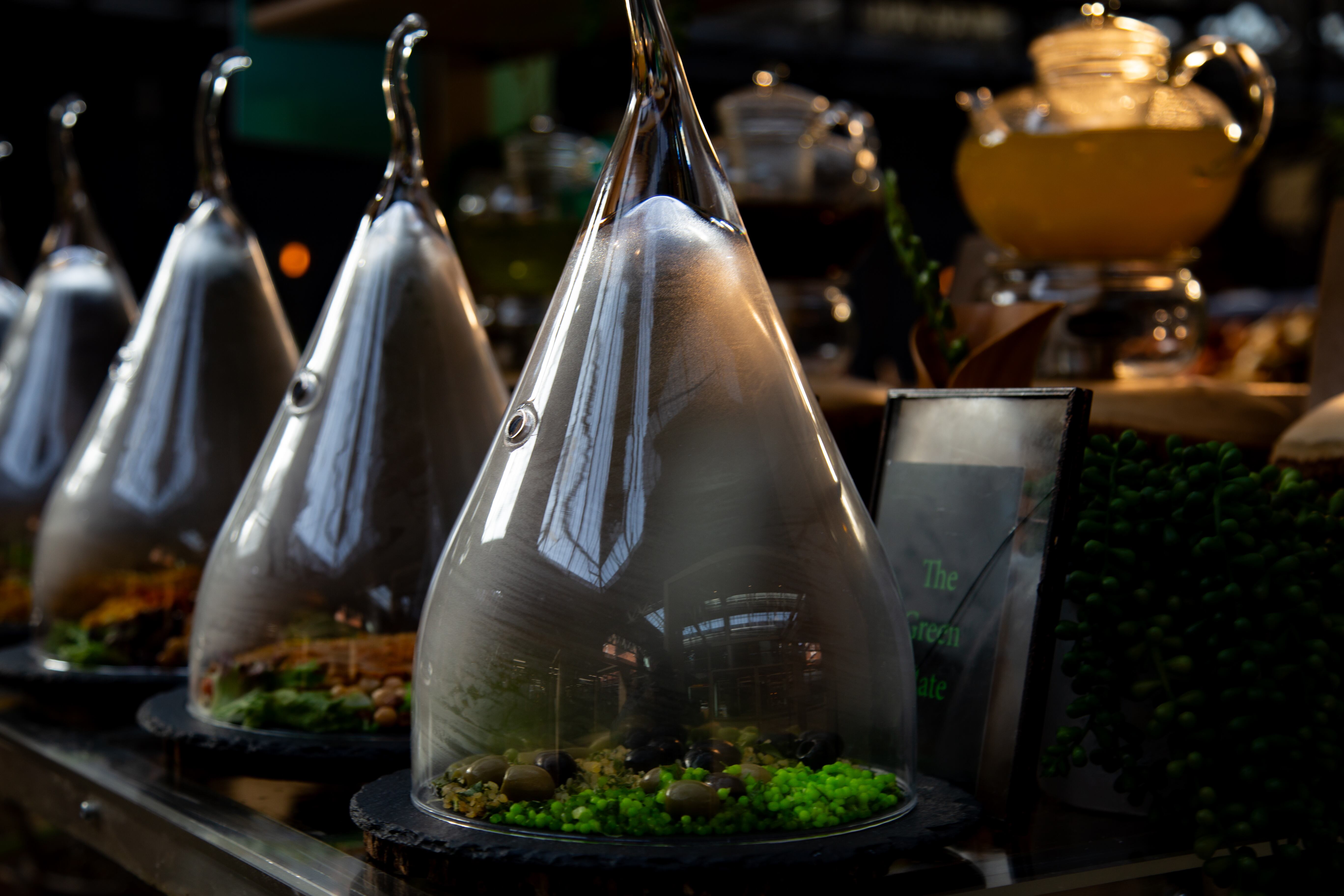 A row of teardrop-shaped glass containers displaying food items, placed on a counter with soft lighting. London, Great Britain