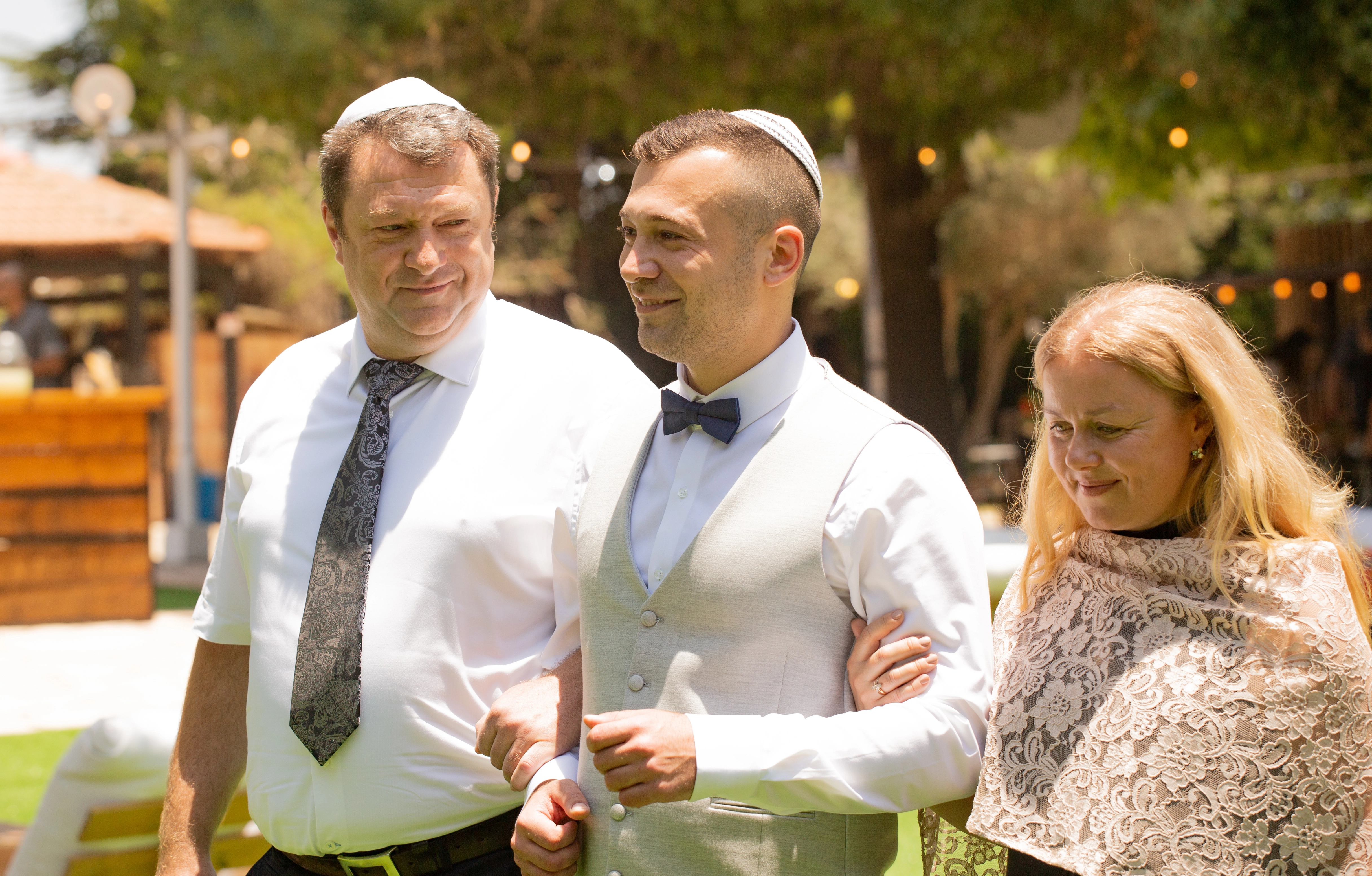 A groom walks arm-in-arm with his parents, sharing a joyful moment under the sunlight.Jerusalem, Israel