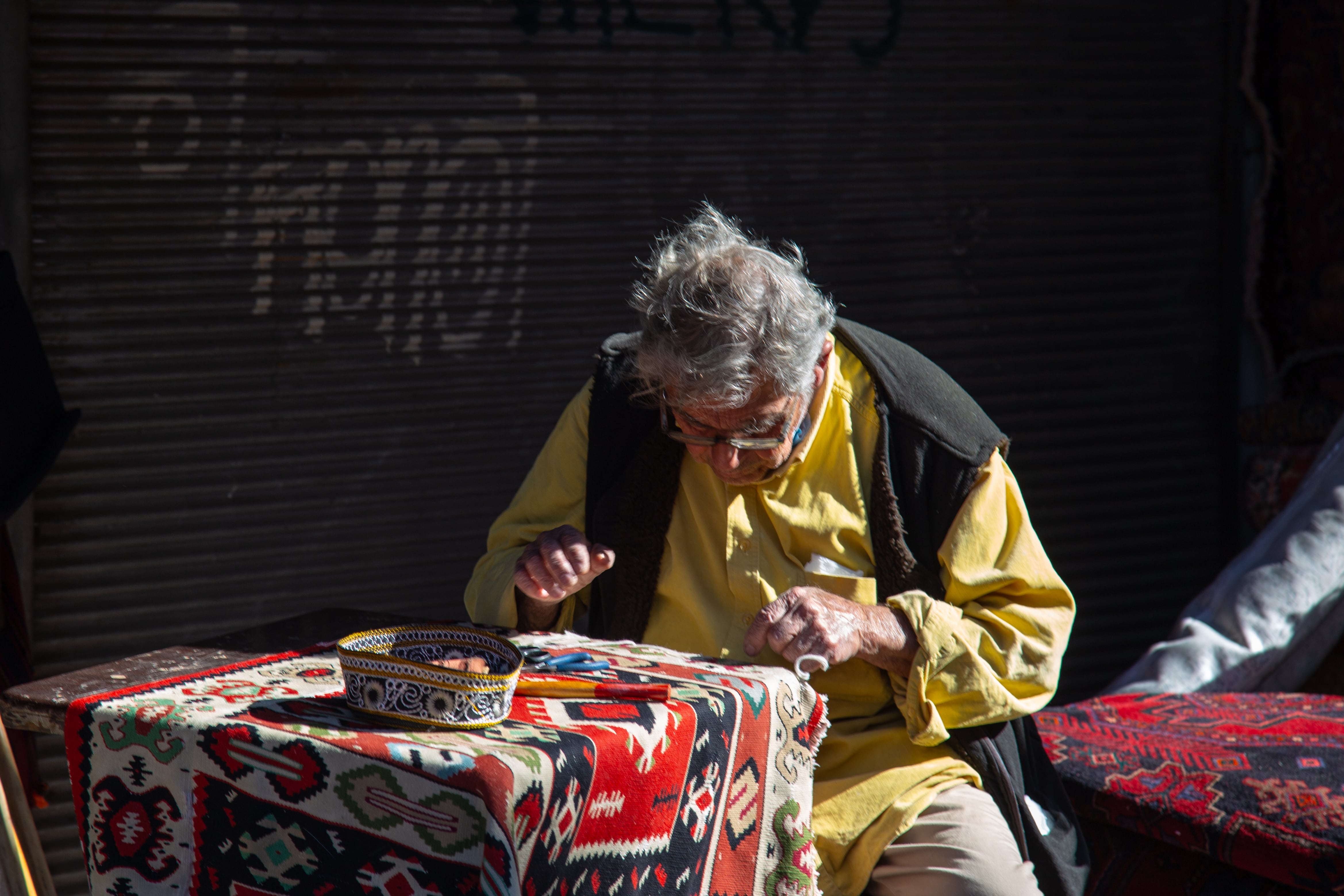 An elderly man tends to colorful threads at Jaffa Flea Market, showcasing quiet dedication amidst the bustle. Tel Aviv Flea Market, Israel