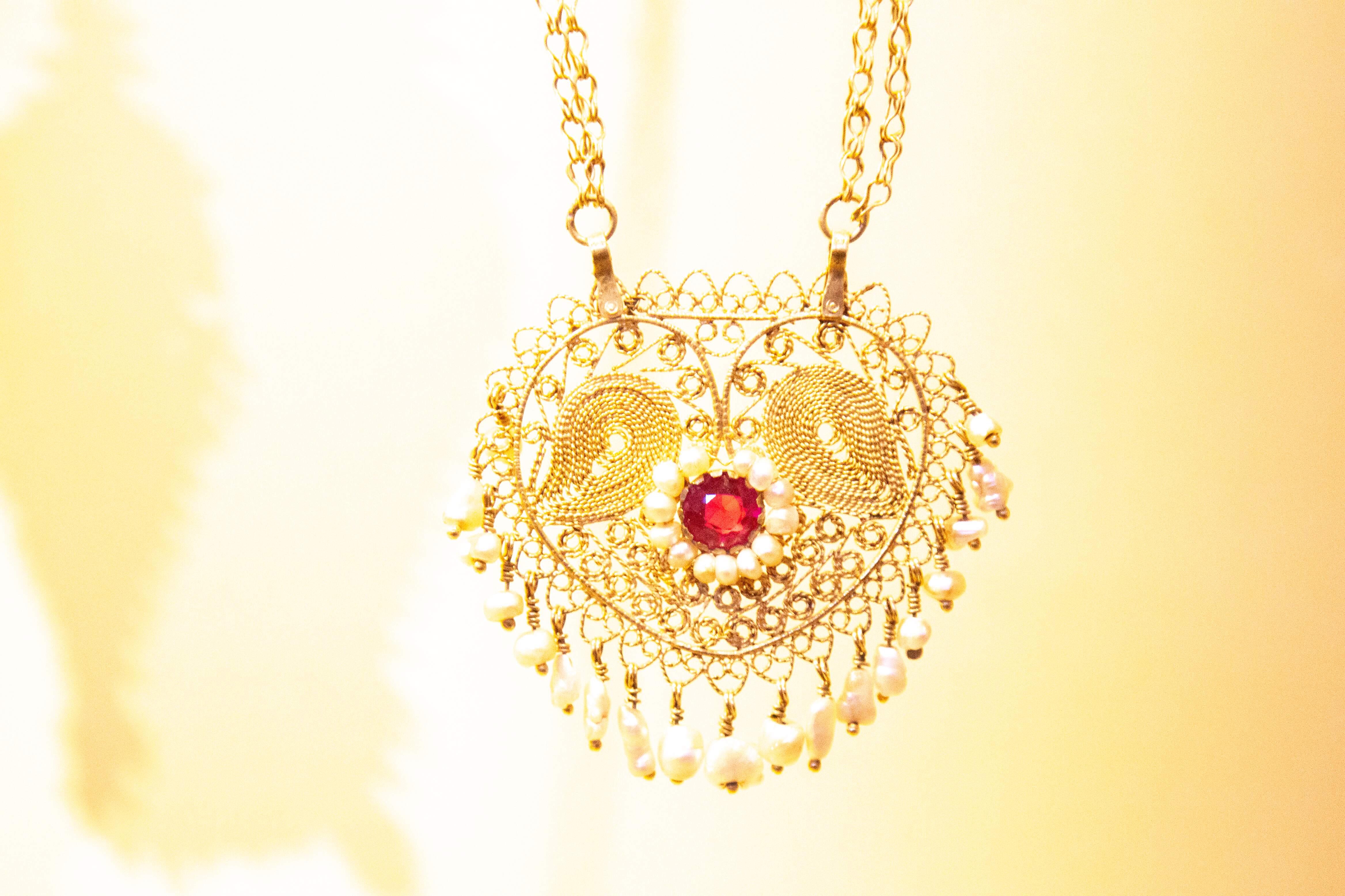 A detailed gold necklace featuring a red gemstone at the center, surrounded by intricate filigree and pearls. Museum of Israel Jerusalem, Israel