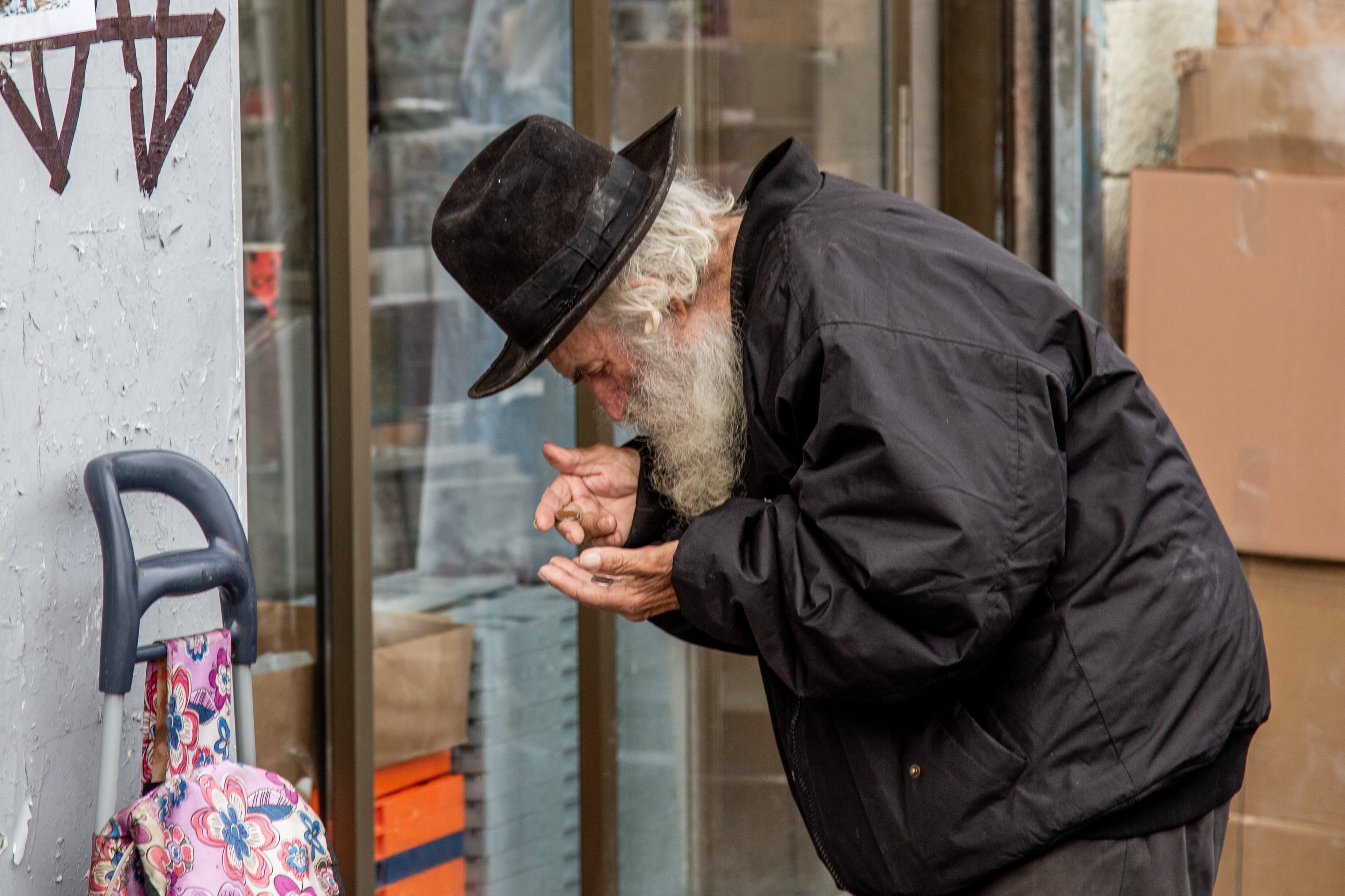 An elderly man in a black coat and hat leans forward in a thoughtful gesture on a street in Jerusalem. Jerusalem, Israel