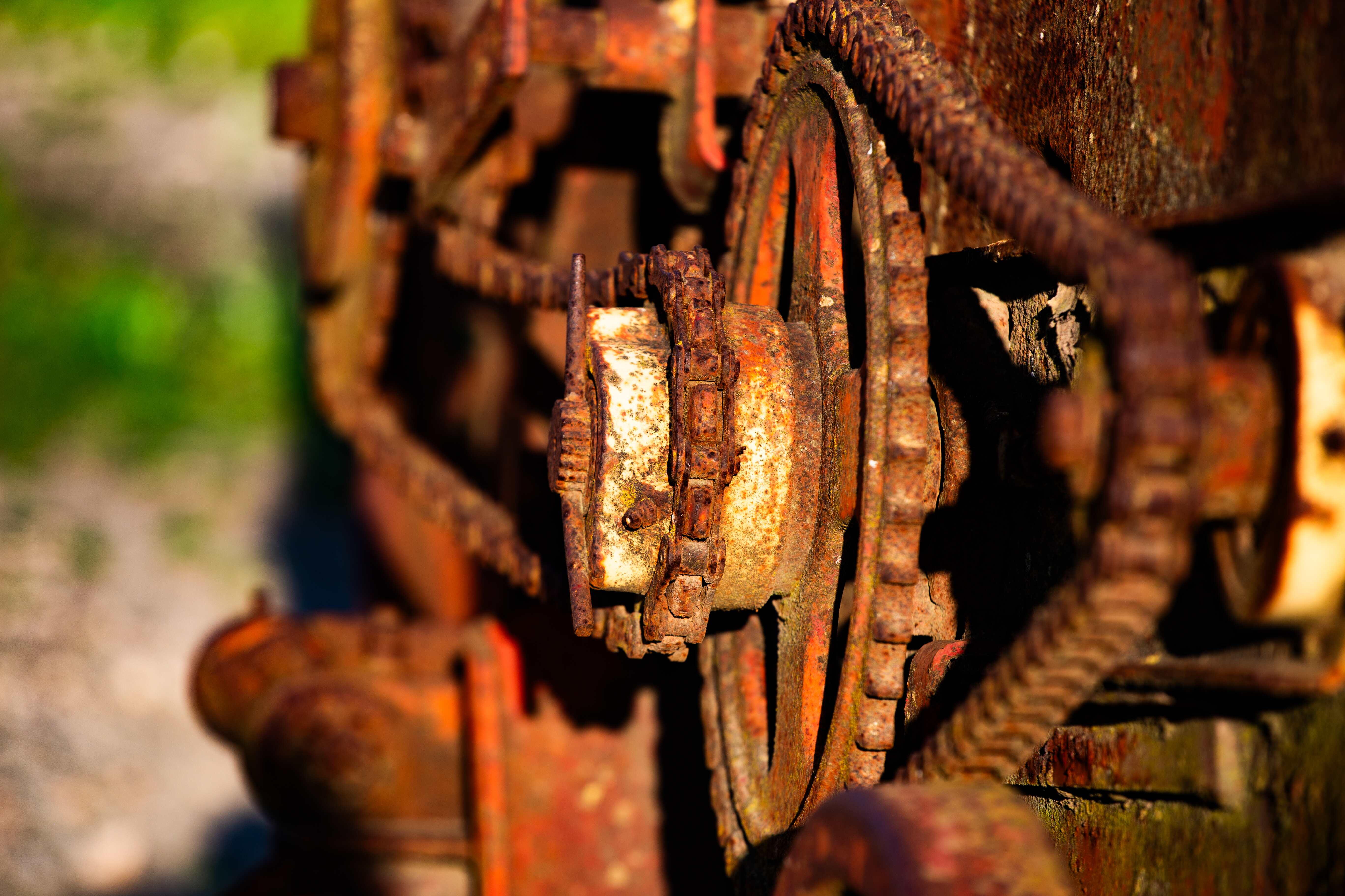 Close-up of rusted gears and chains on old machinery, with a background of blurred greenery. Ahula Lake, Israel