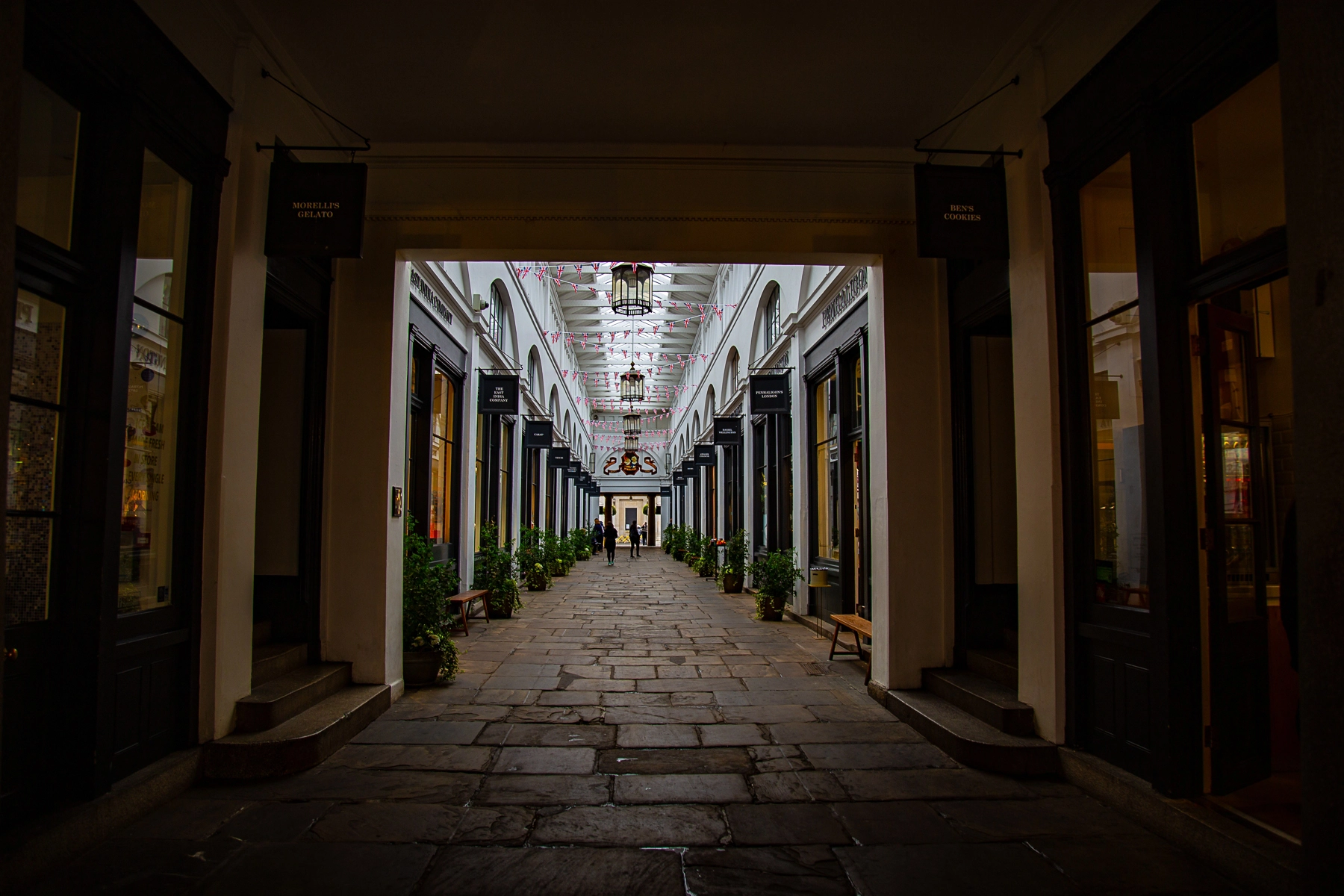 A view down a historic covered passageway in London, lined with shops and decorated with hanging lights. London,Great Britain