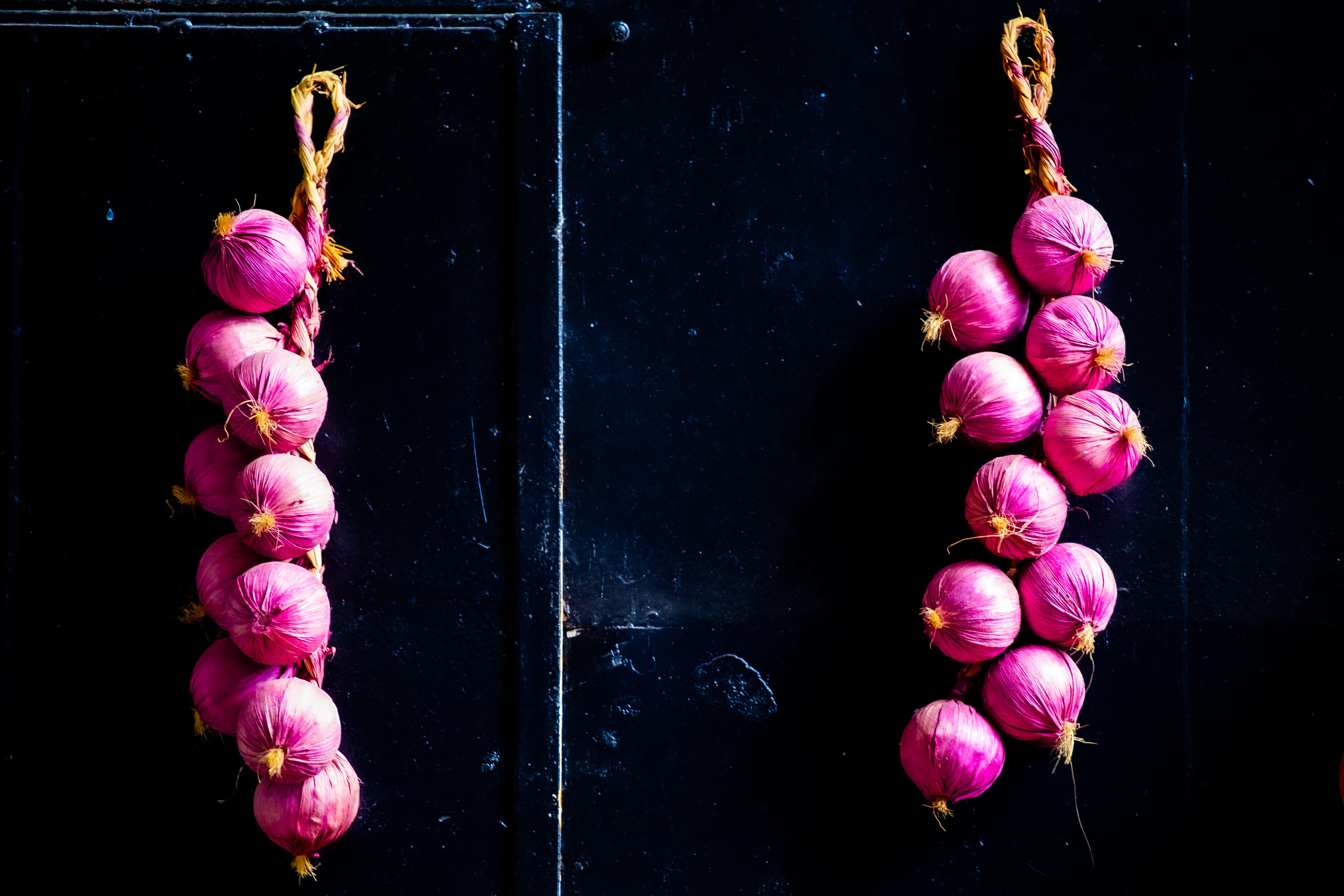 Two braids of vibrant red onions hanging against a dark, textured background, creating a bold contrast. Tel Aviv, Israel