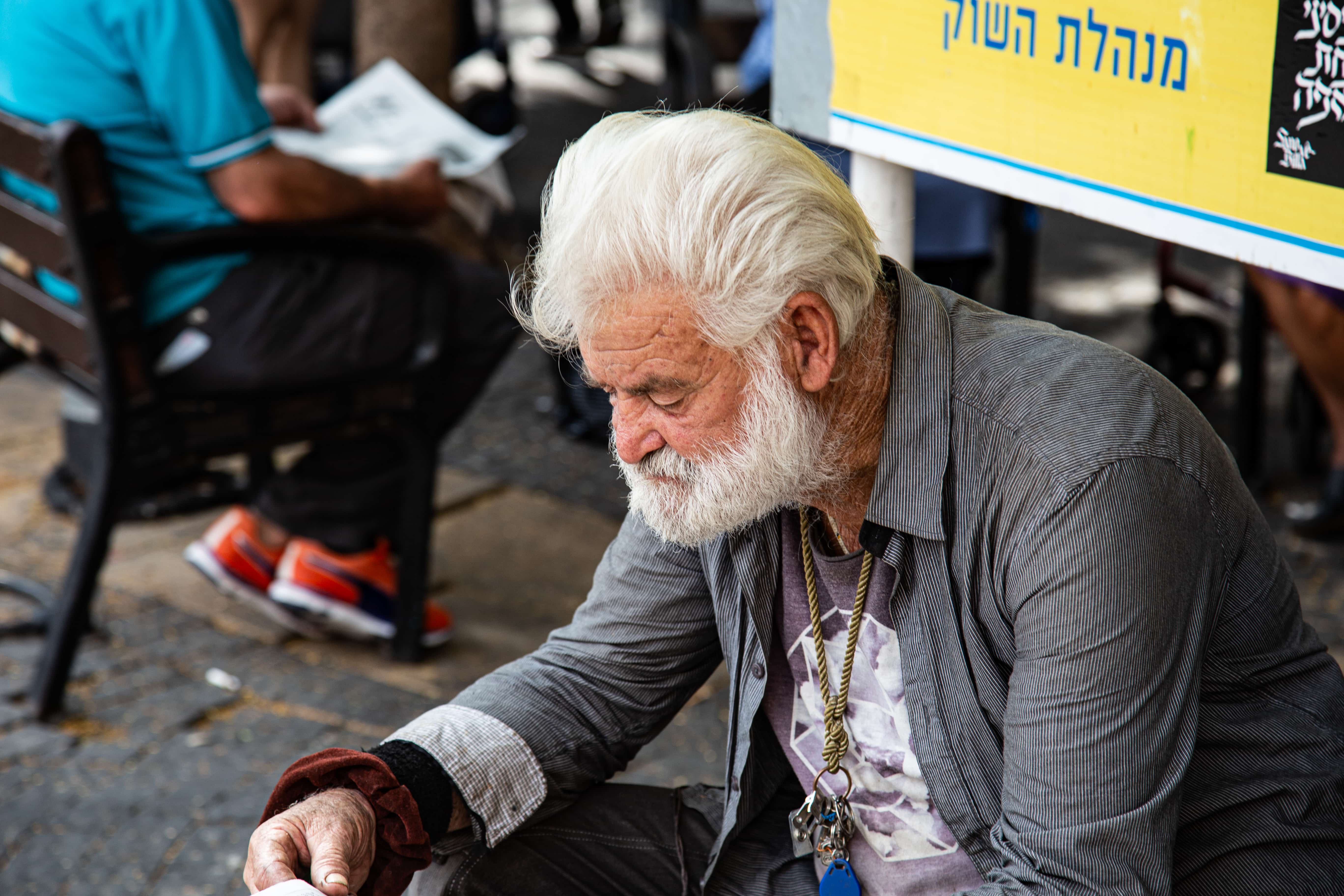 An elderly man sits at Carmel Market, deep in thought, offering a glimpse into a quiet personal moment. Carmel Market, Tel Aviv, Israel