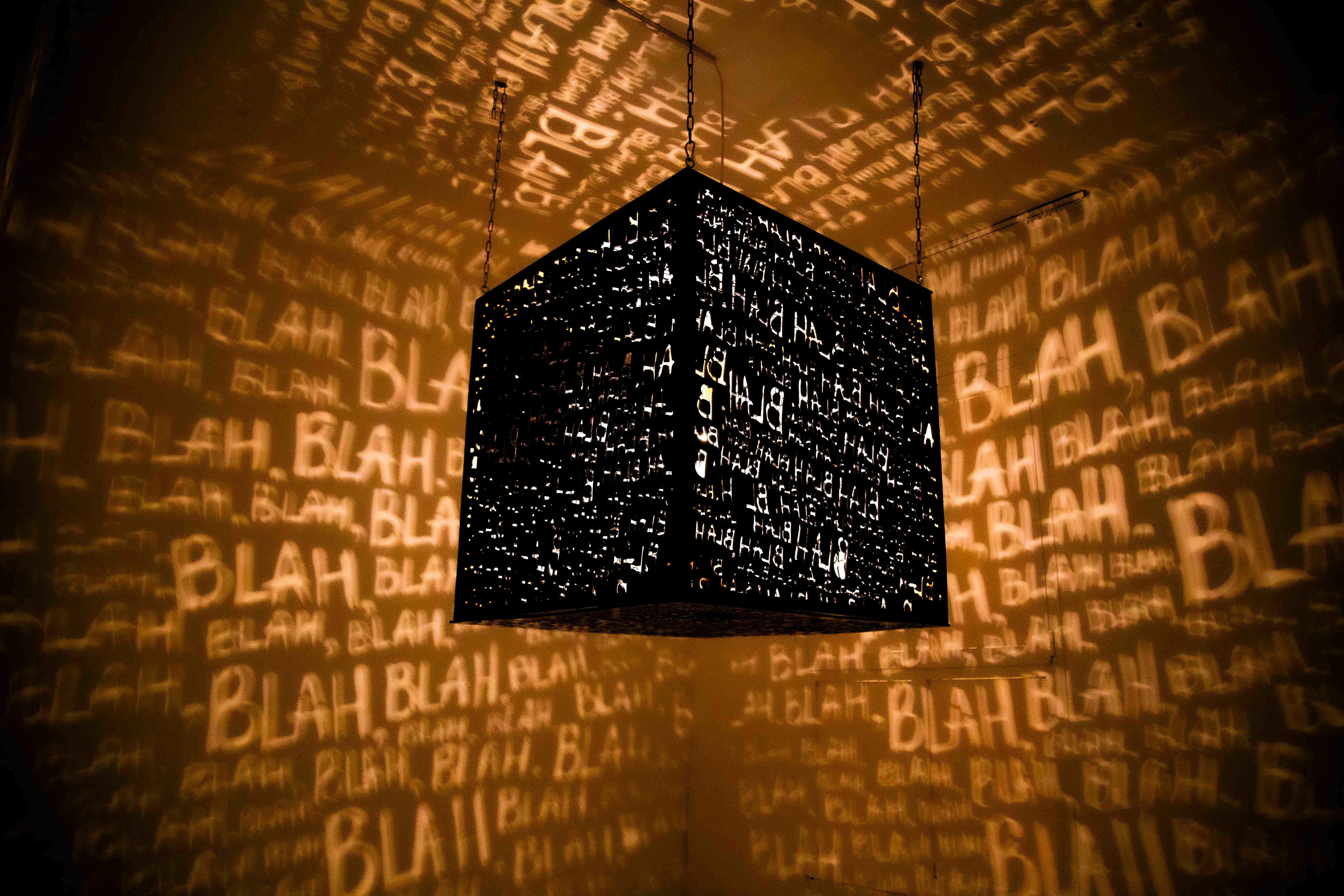 A cube-shaped lamp projecting the word "BLAH" repeatedly onto the walls in dramatic lighting.