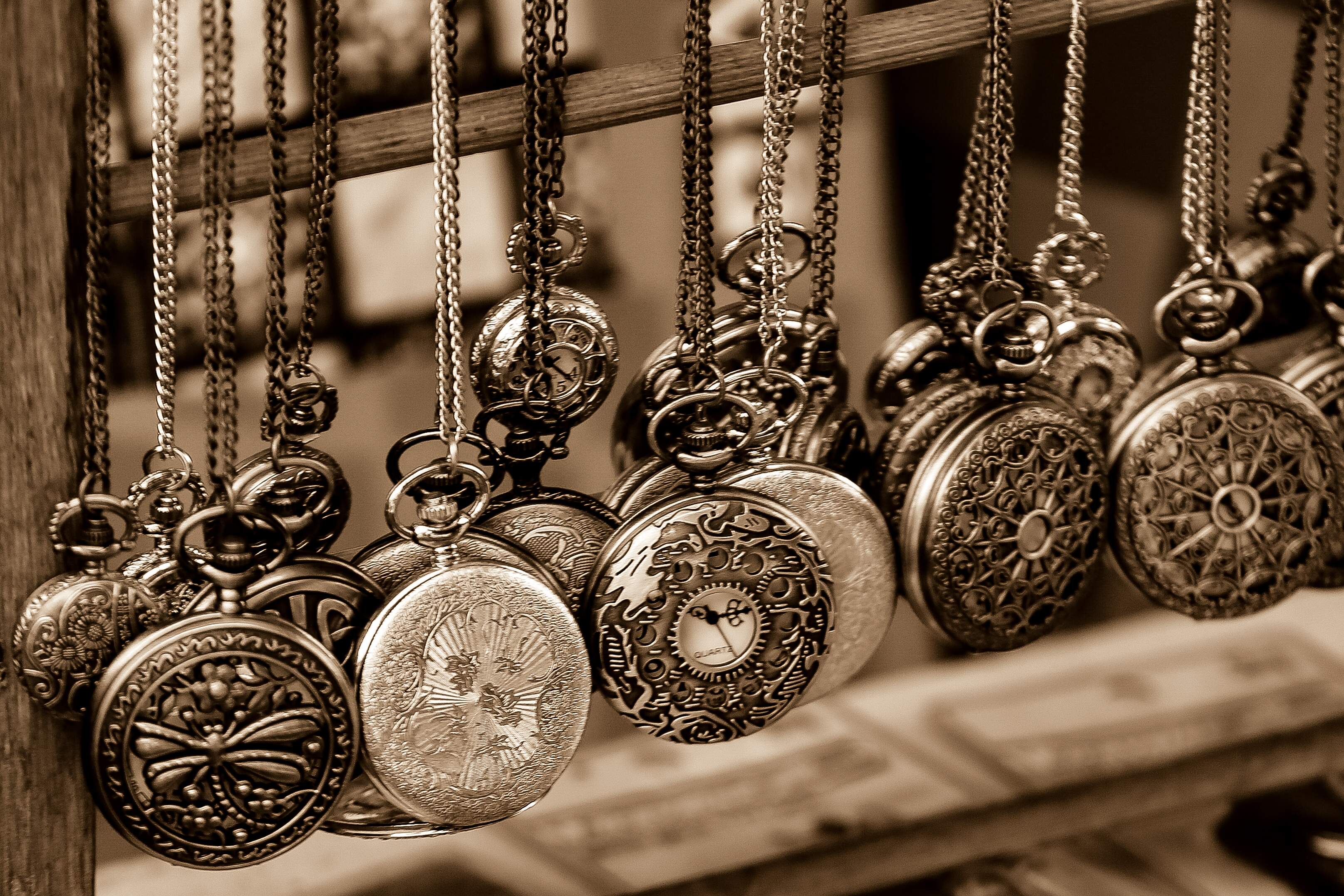 A sepia-toned display of vintage pocket watches with intricate designs hanging from chains at a market stall. Jaffo Flea Market, Israel