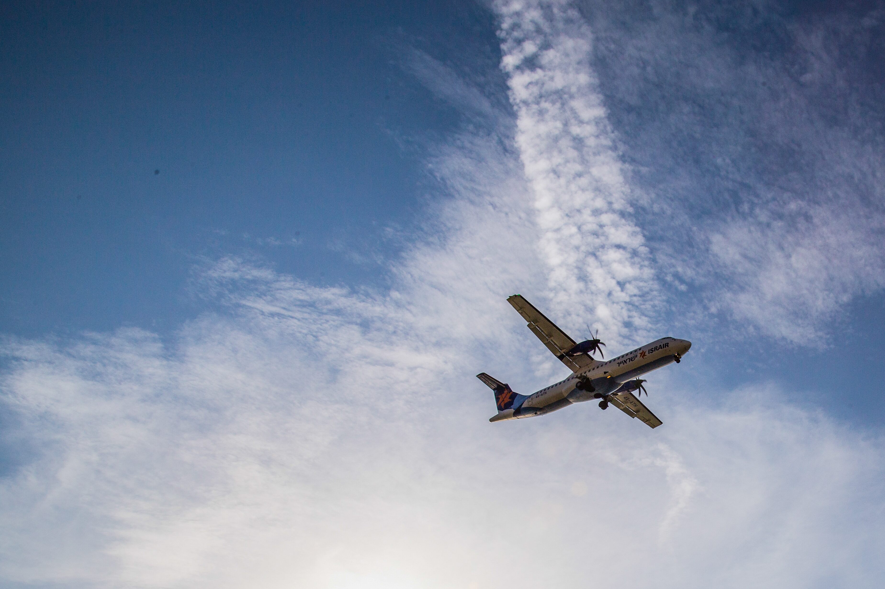 An Israir propeller plane flying low over Tel Aviv, set against a bright sky with light cloud formations. Tel Aviv, Israel