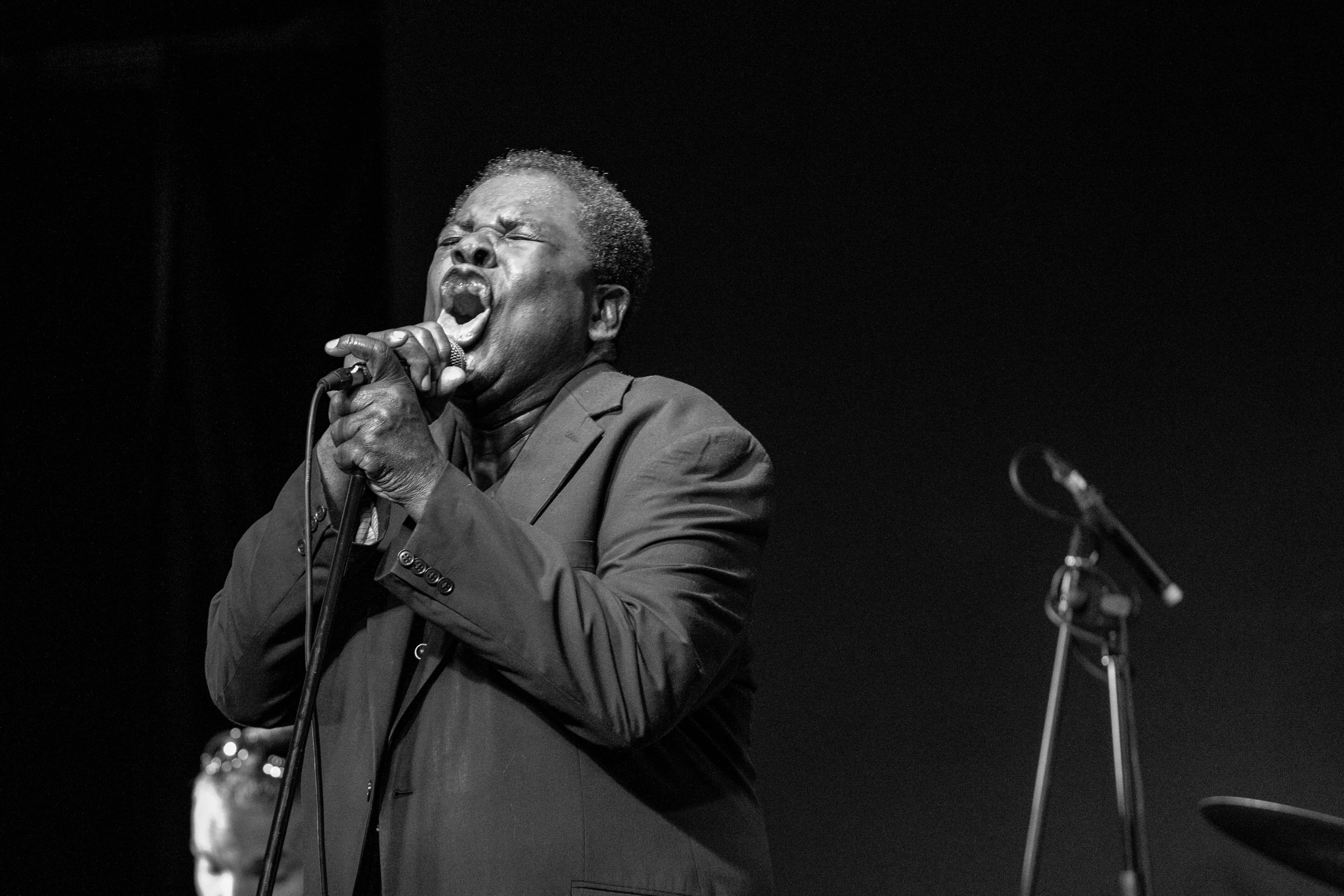 Roy Young passionately singing into a microphone during a live performance, captured in black and white. Tel Aviv, Israel