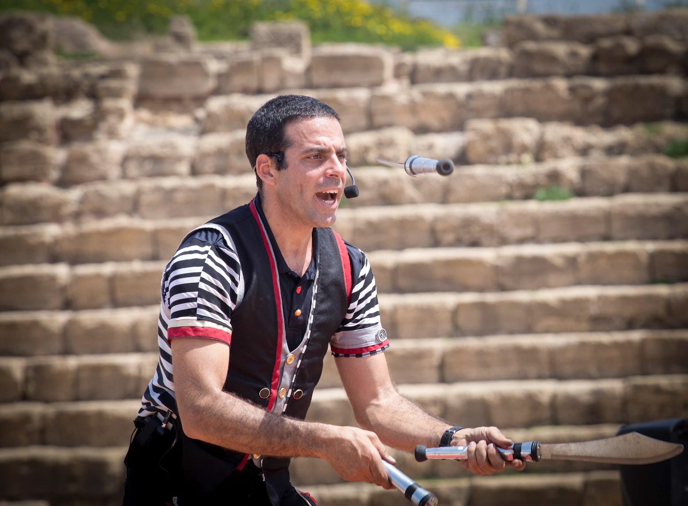 A performer juggles knives at the Caesarea amphitheater, captivating the crowd against the historic stone backdrop. Caesarea, Israel