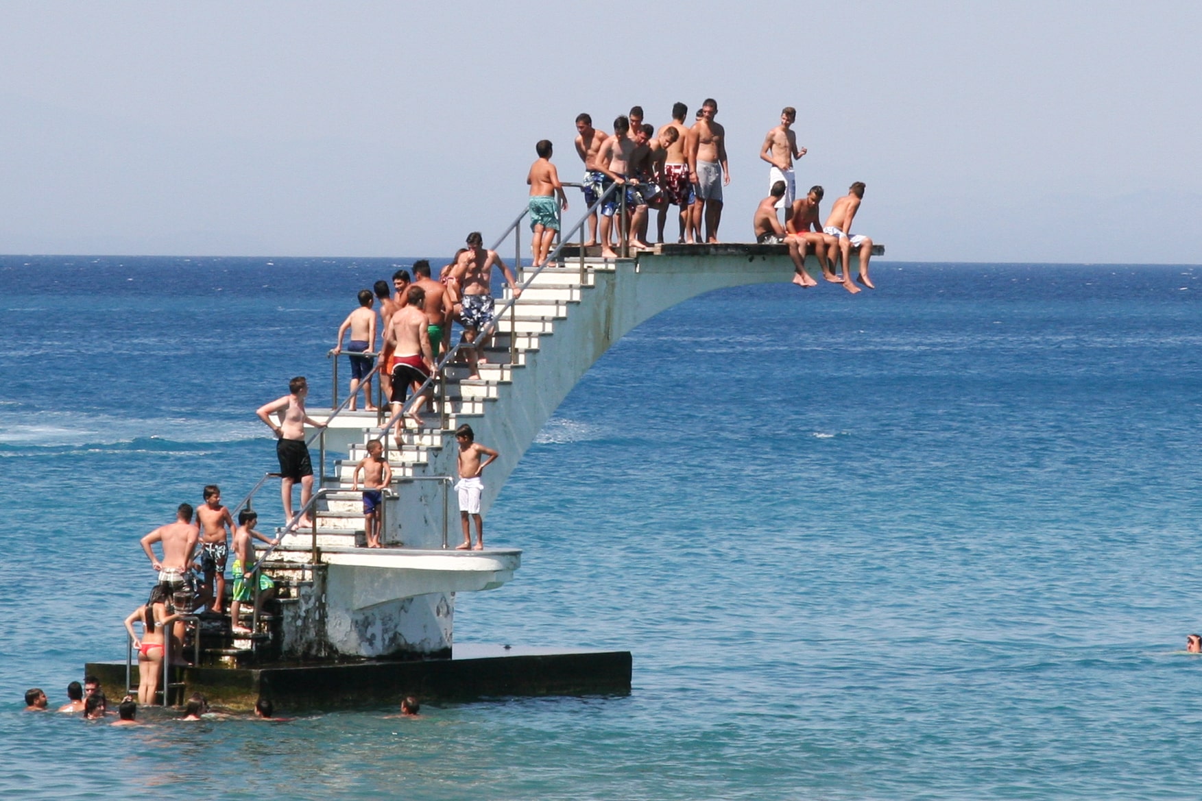 Beachgoers gather on a high diving platform over clear waters in Rhodes, Greece, enjoying a sunny day. Rhodes City, Greece