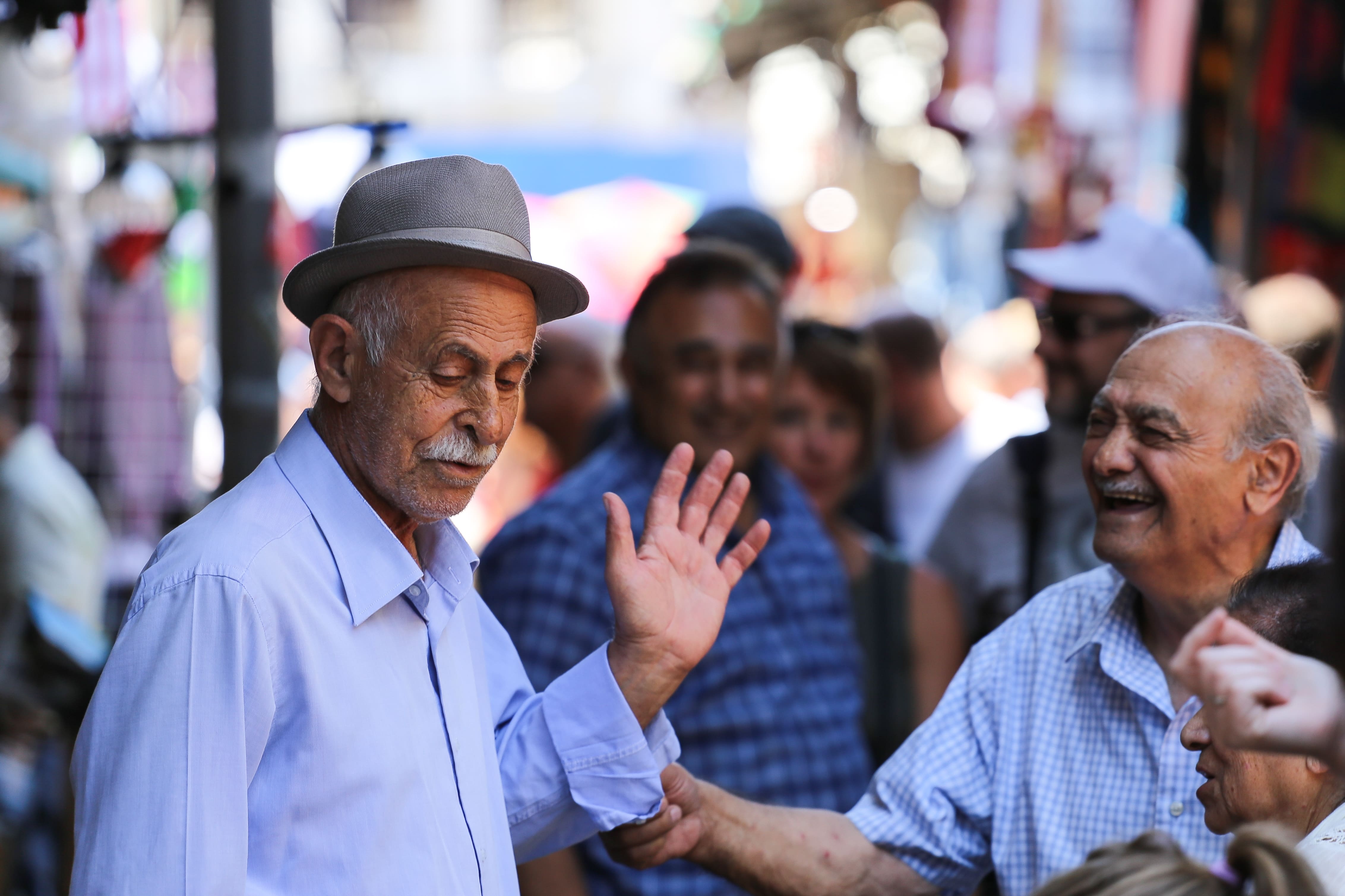 An old man waves, surrounded by smiling friends at Tel Aviv Flea Market, capturing camaraderie and joy. Jaffa Flea Market, Tel Aviv, Israel