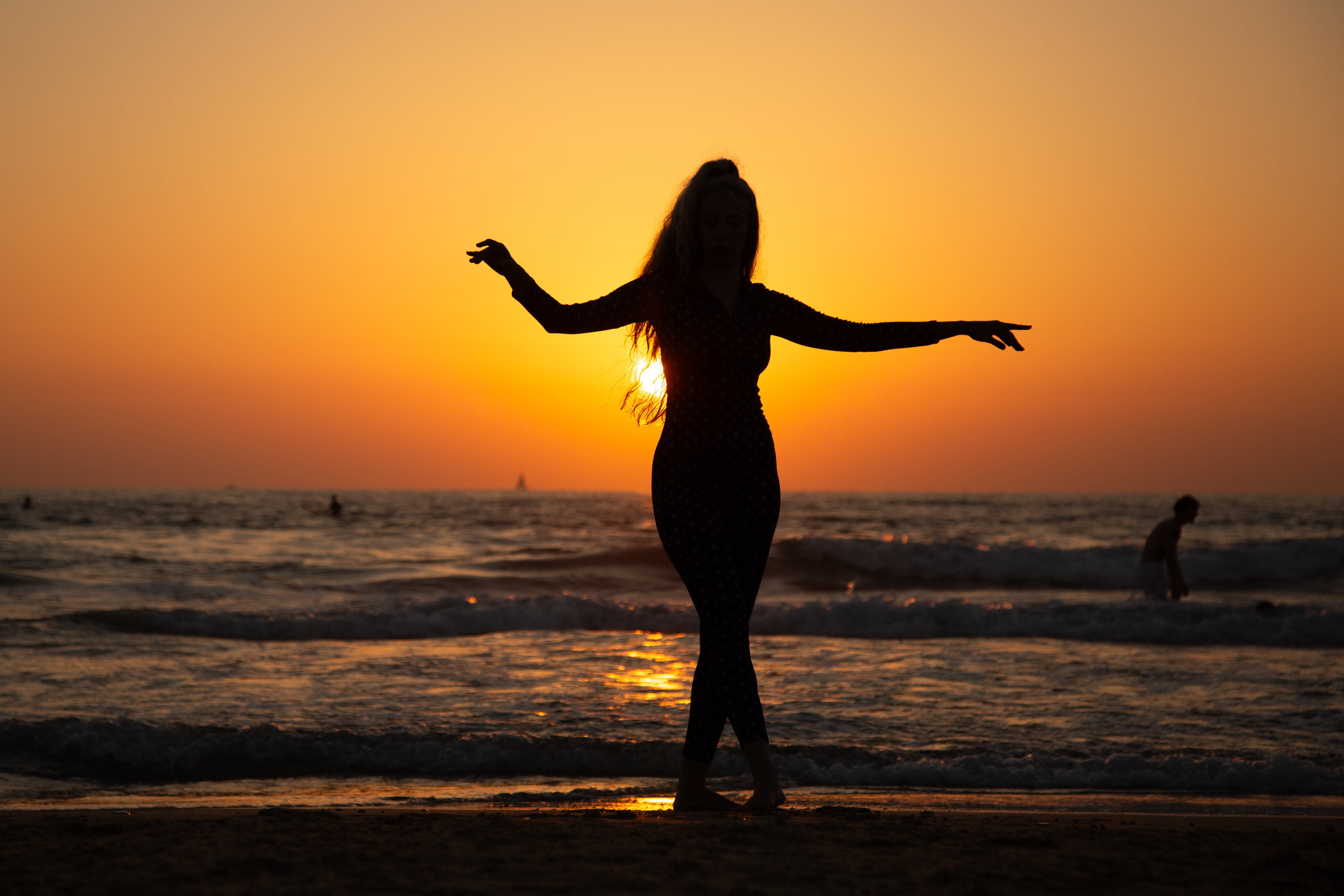 A woman silhouetted against a golden sunset, performing a graceful dance on the beach. Tel Aviv, Israel