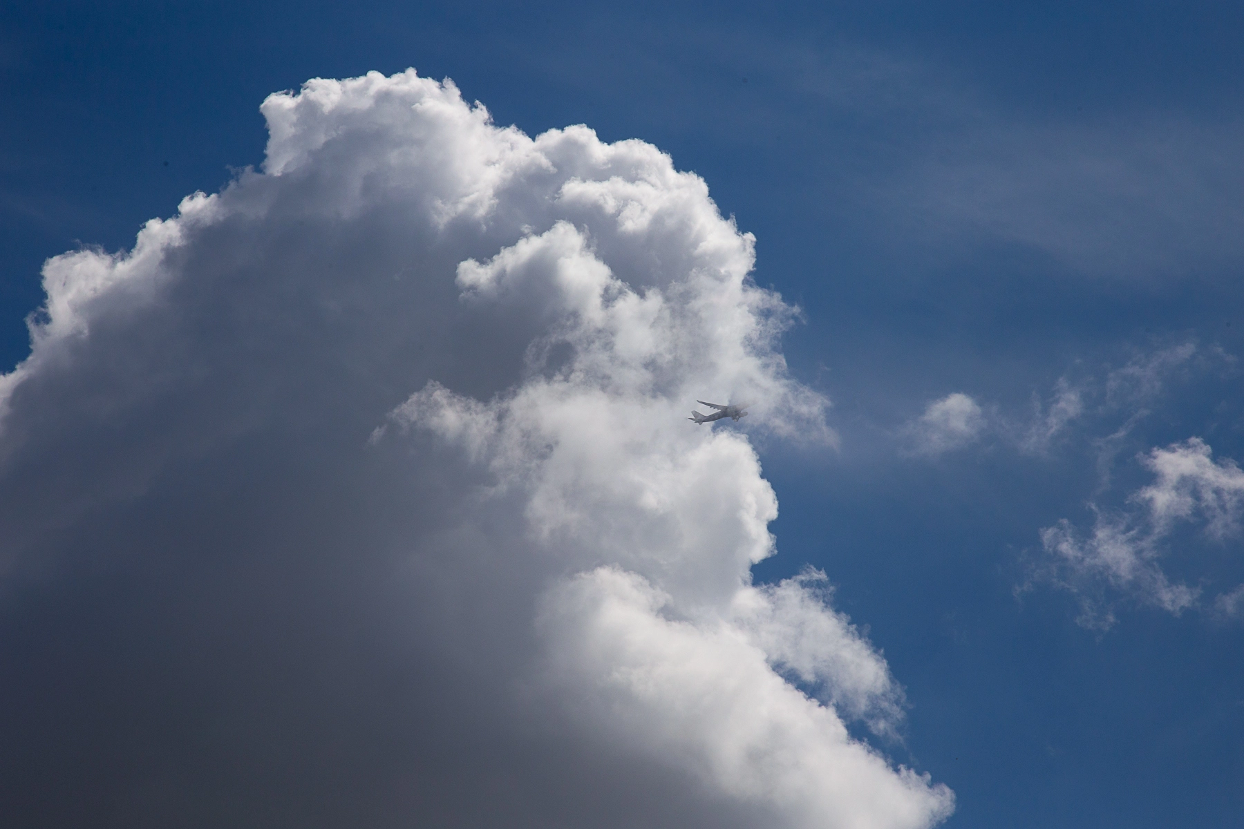 An airplane is captured flying into a large fluffy cloud with a bright blue sky in the background. London,Great Britain