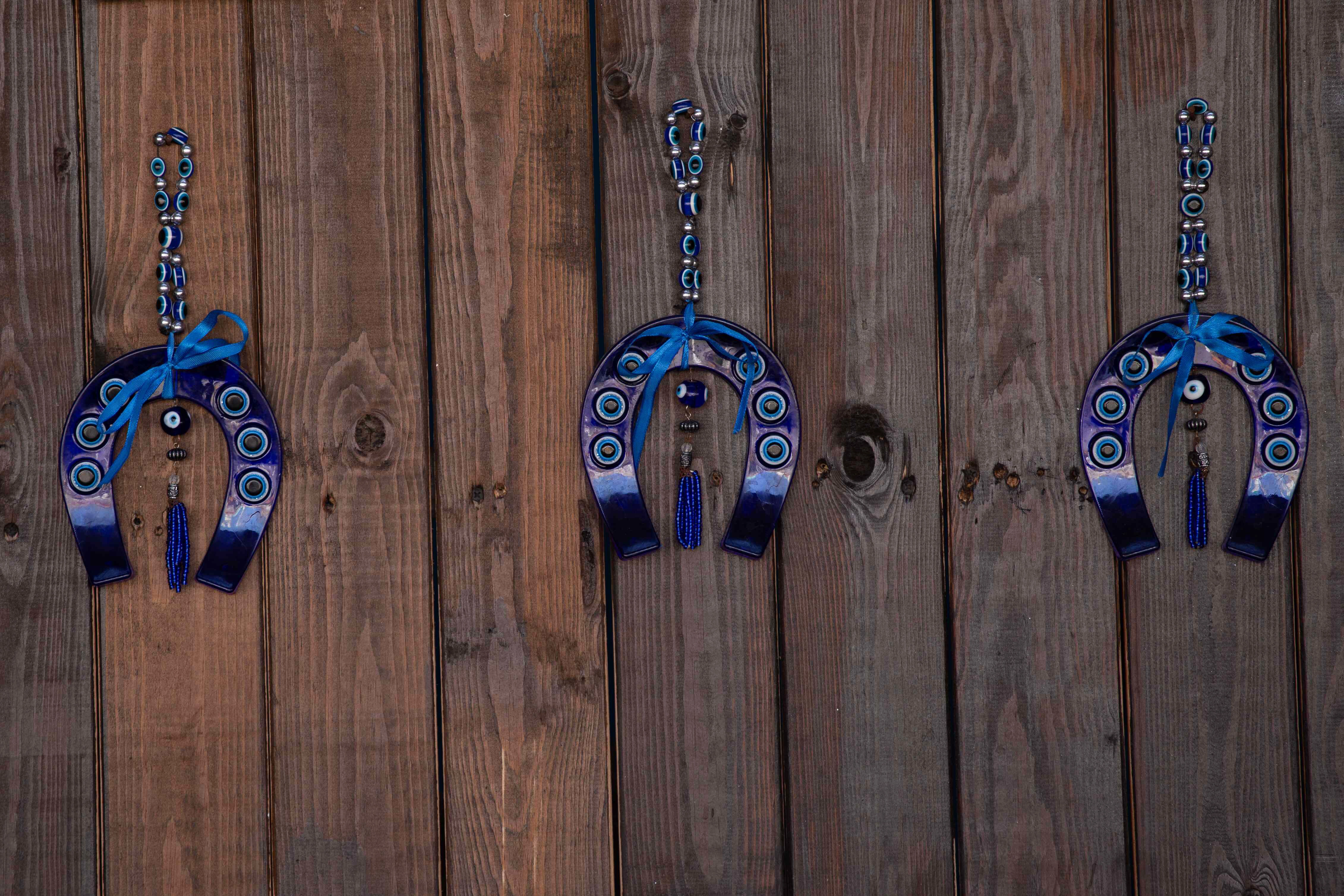 Three decorative horseshoes adorned with blue evil eye beads hang on a rustic wooden wall. Acco, Israel