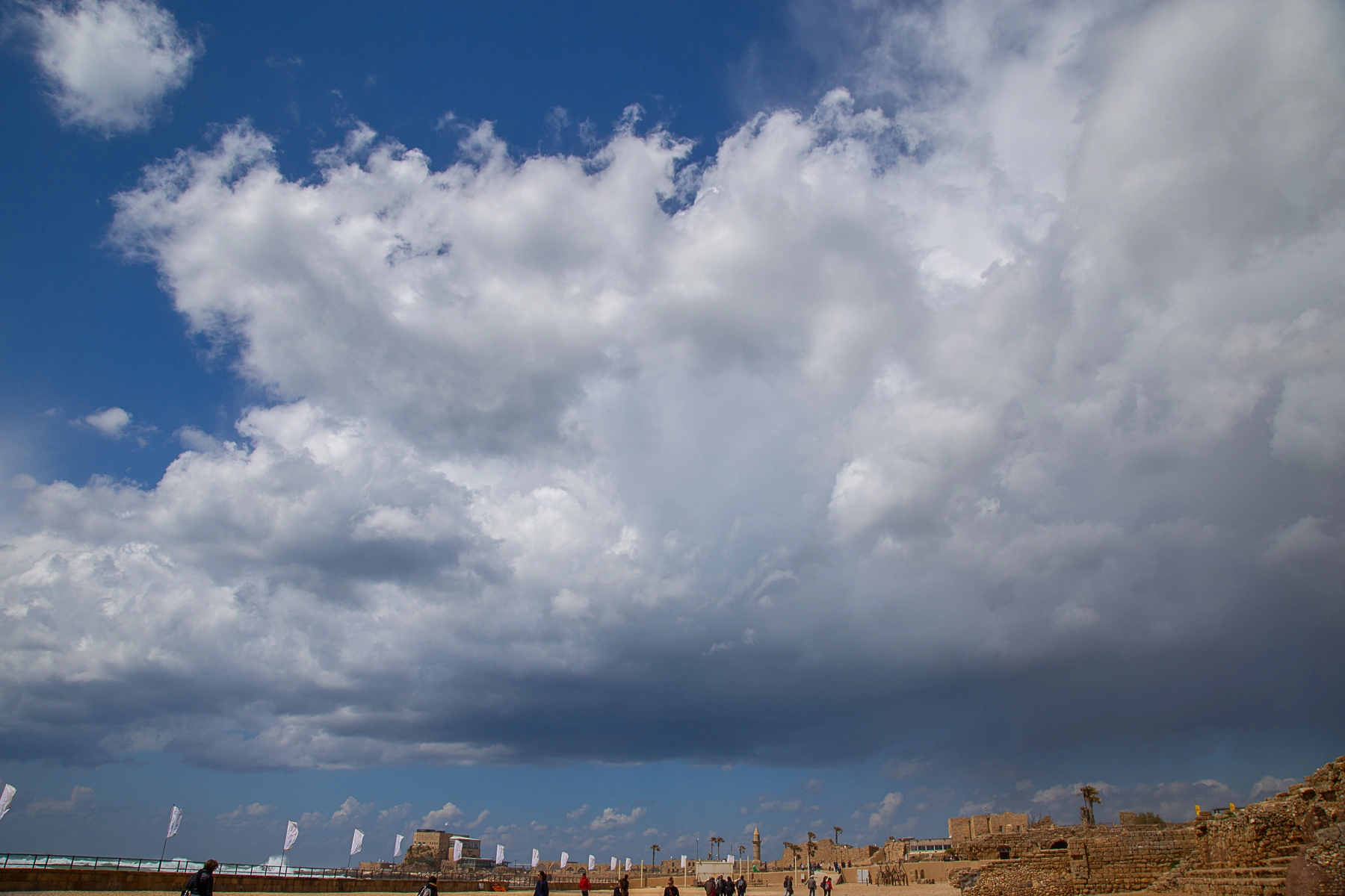 A view of dramatic clouds over the ancient city of Caesarea with a hint of sunlight breaking through. The coastline and historical structures are visible. Caesarea,Israel