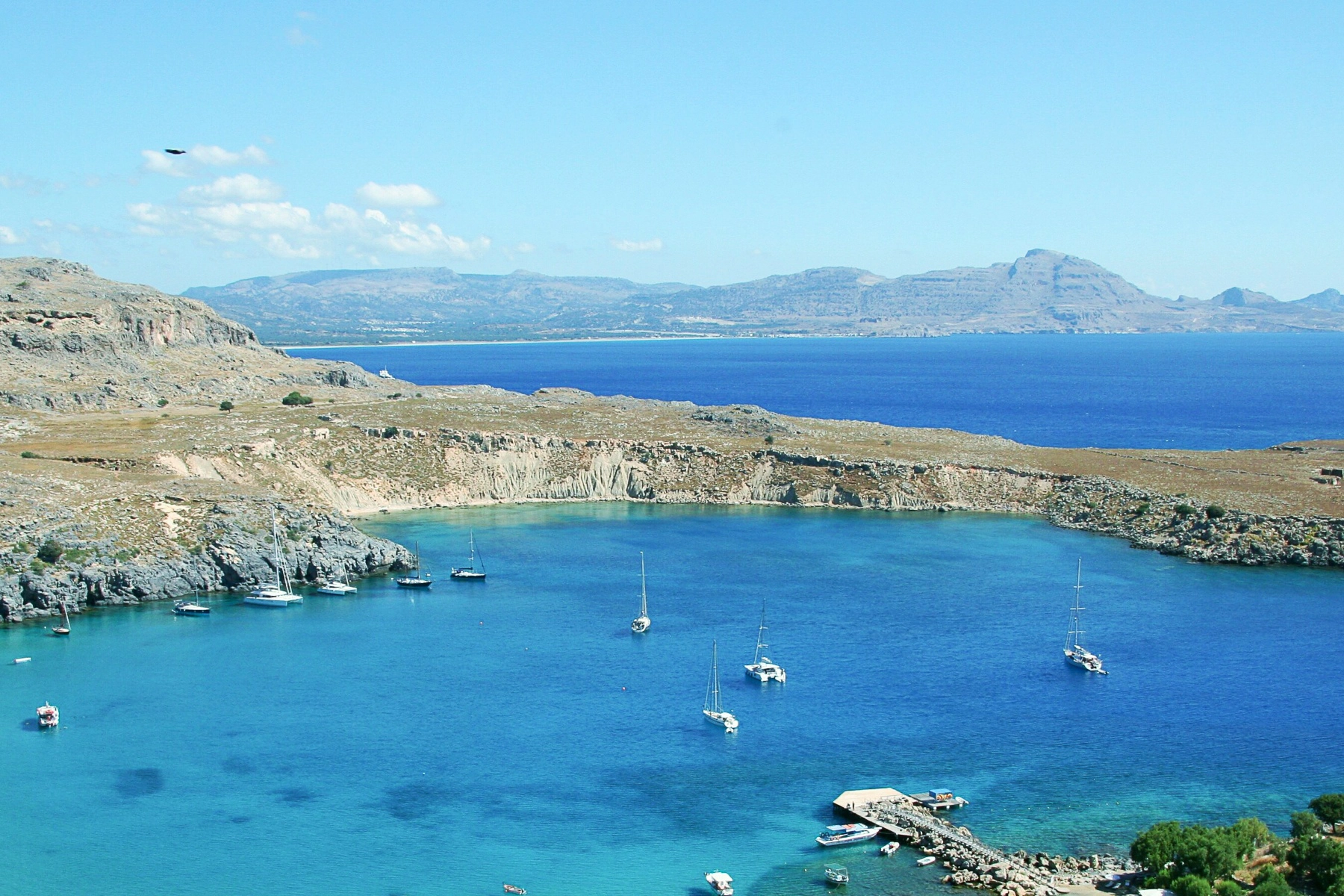 A scenic view of Lindos Bay with sailboats anchored in crystal-clear turquoise water. Lindos, Greece