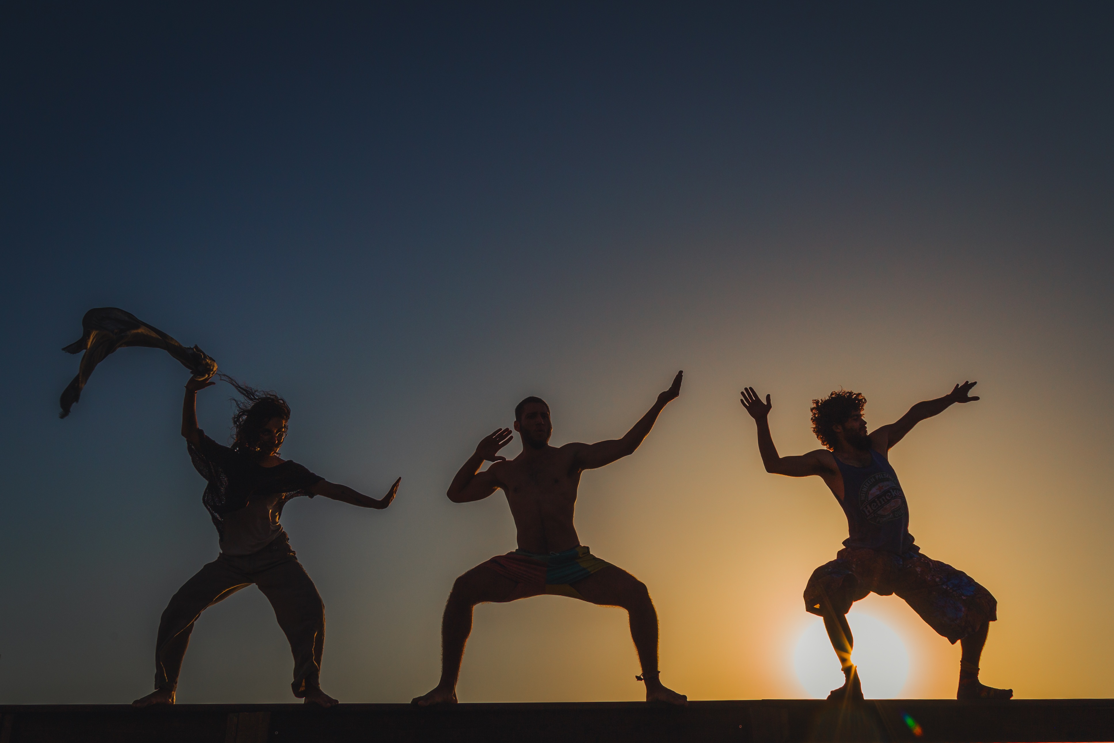 Three performers striking playful, dynamic poses, silhouetted by the setting sun. Mitzpe Ramon, Israel