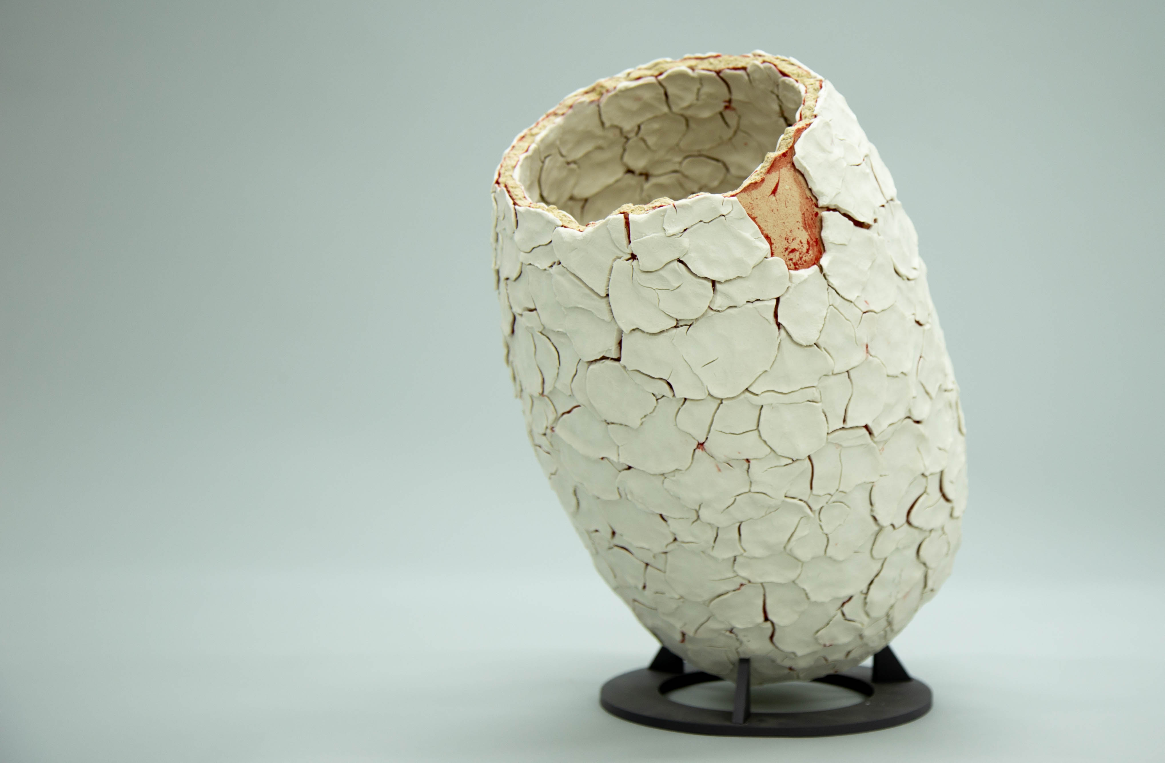 A textured ceramic vase with a cracked, layered surface, placed on a minimalist stand.