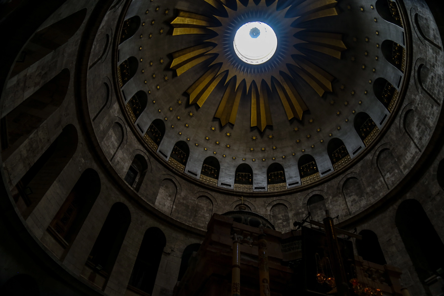 Interior view of a church dome with a skylight, featuring gold accents and star motifs against a gray stone structure. Jerusalem.Israel