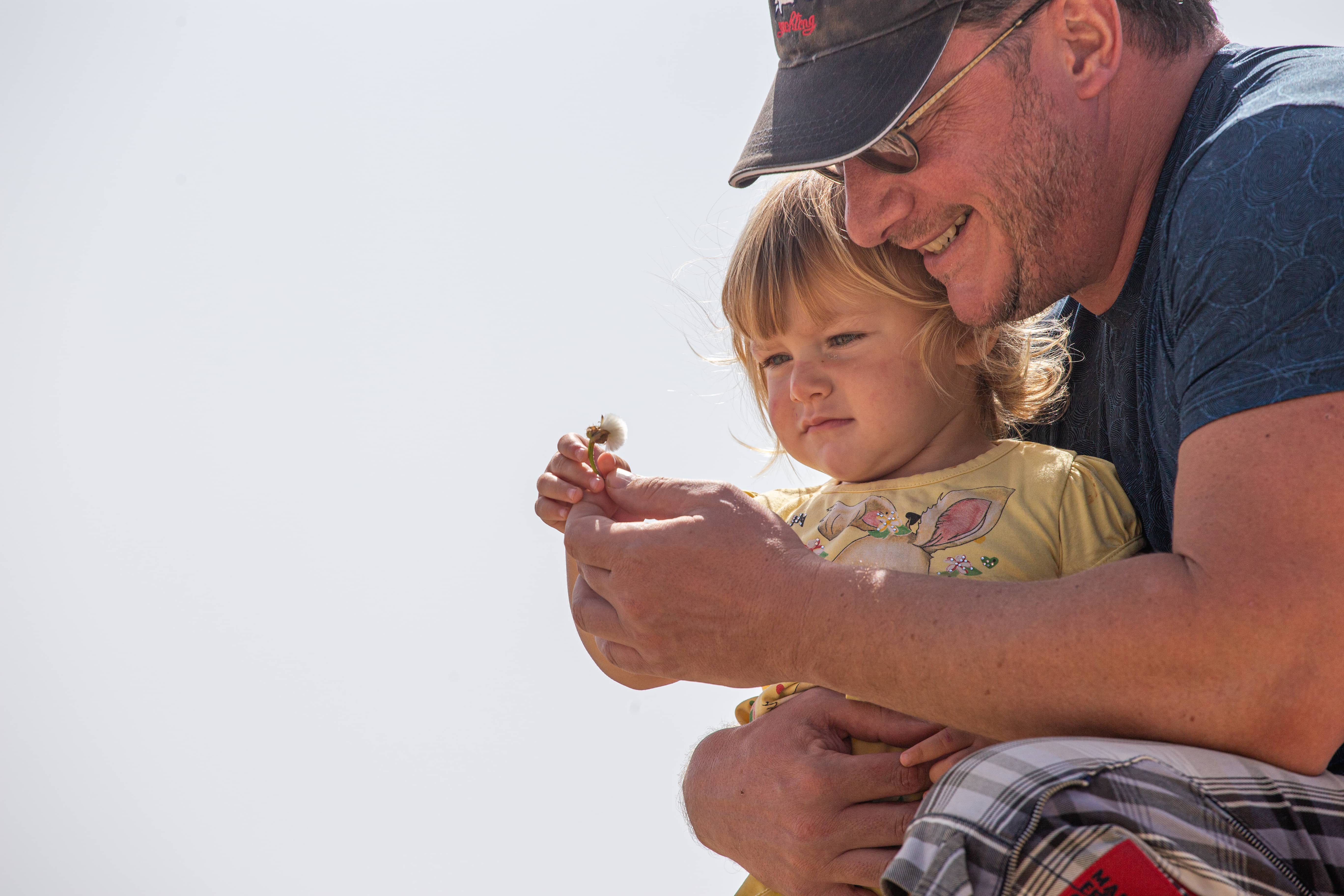 A father smiles while showing a dandelion to his young daughter outdoors. Caesarea, Israel