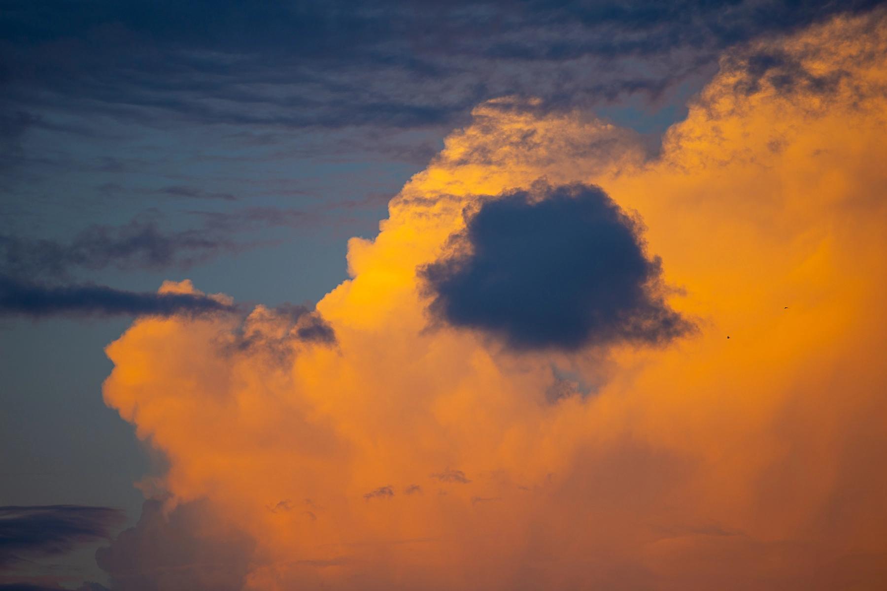 Clouds glowing orange from the setting sun, contrasting against a darker blue sky with wisps of shadowed clouds. Hertzliya, Israel