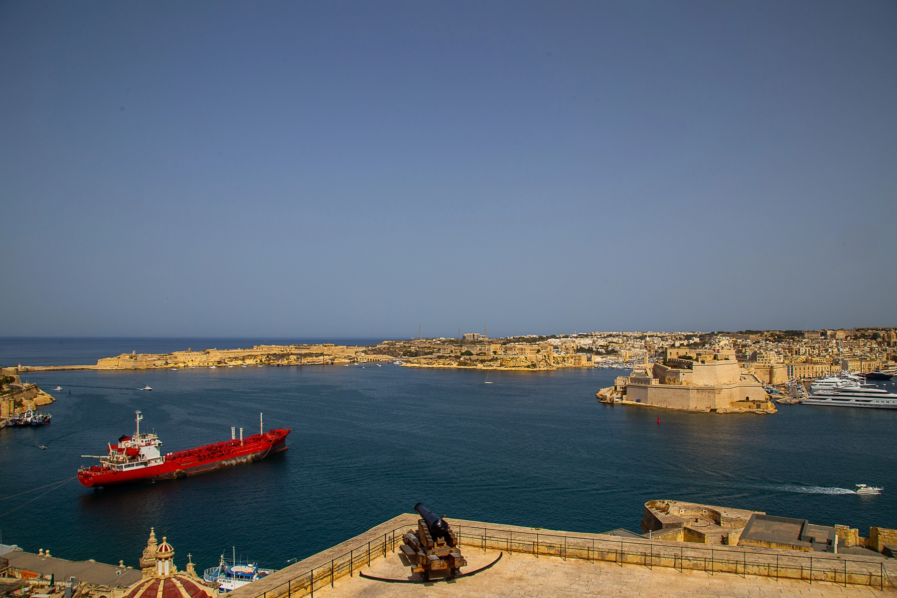 A stunning view of Valetta's harbor with a red ship, fortifications, and clear blue waters. Valetta, Malta