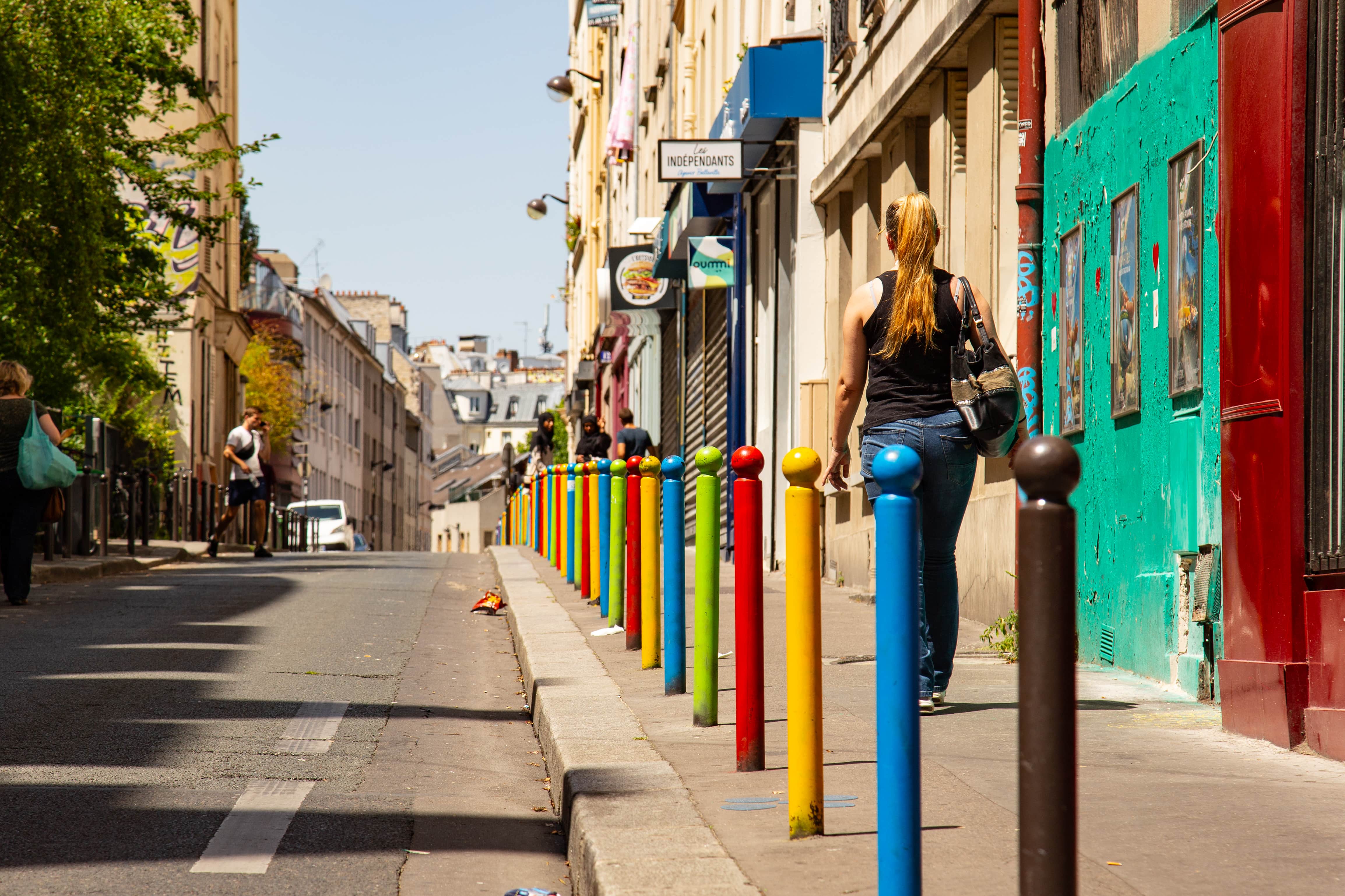 A woman strolls down a vibrant Paris street lined with colorful posts, enjoying the bright, lively atmosphere. Paris, France