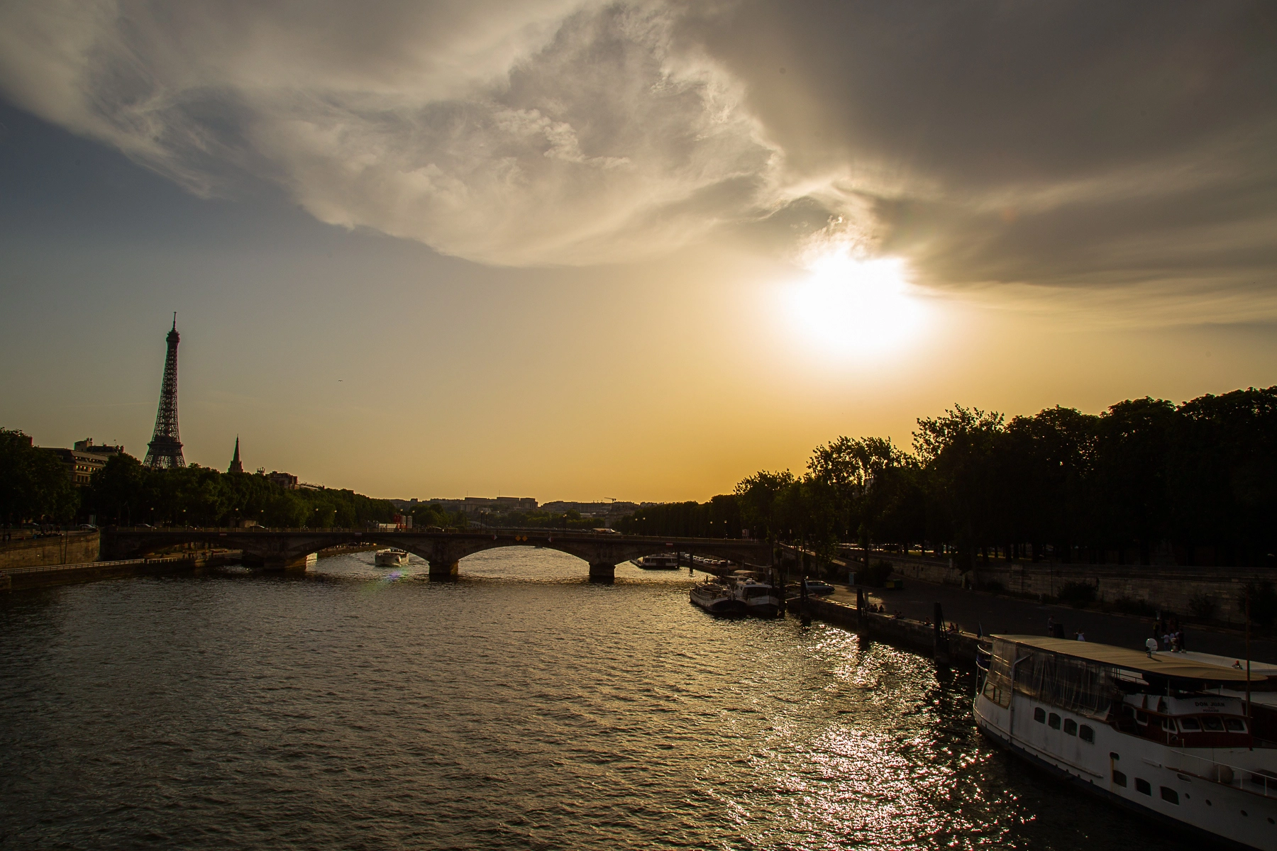 The Eiffel Tower is silhouetted against a golden sunset as the Seine River flows below a picturesque bridge. Paris, France