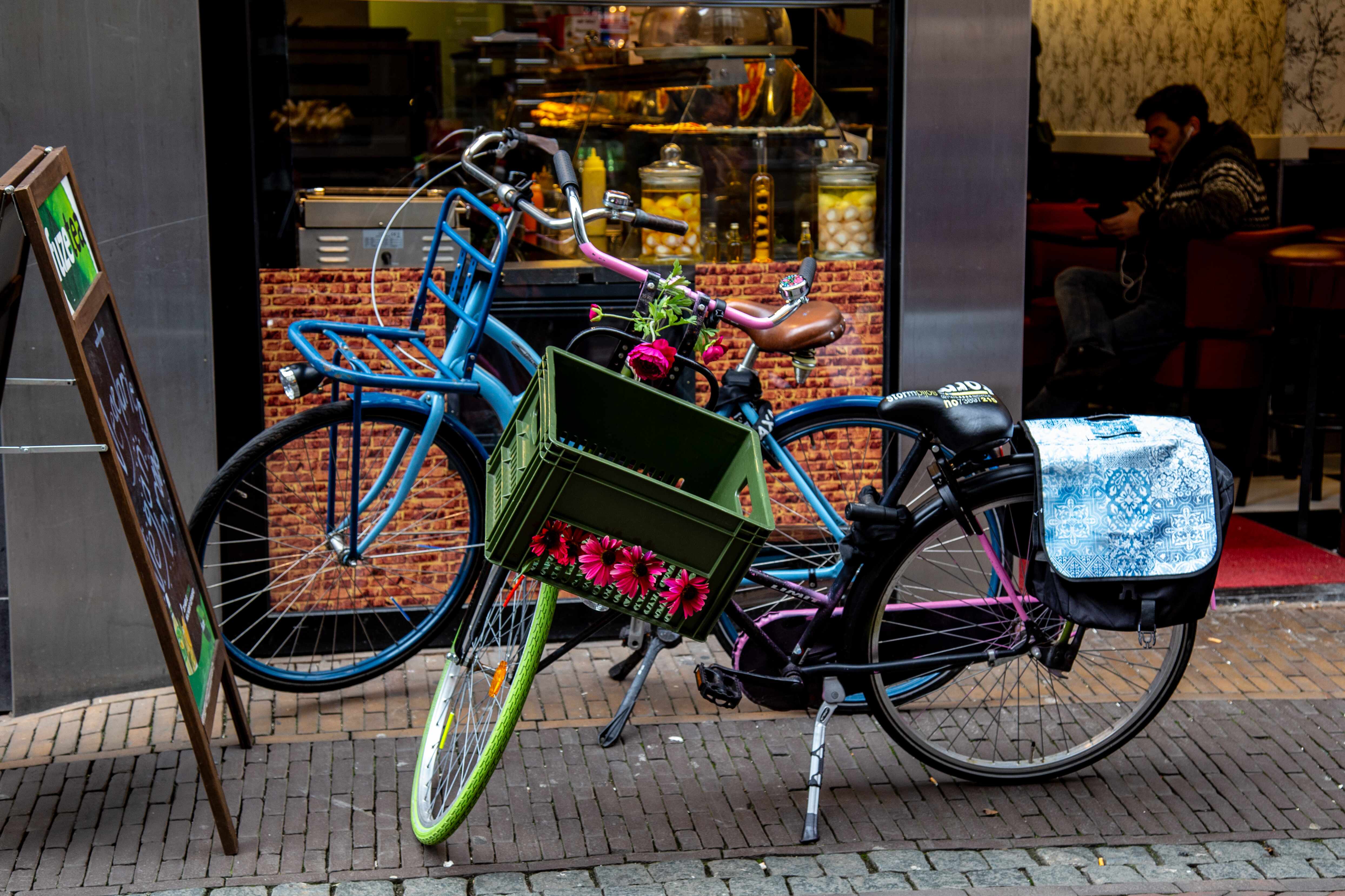 A pair of bicycles, one adorned with flowers, rests outside a café, adding charm to the bustling street. Utrecht, Netherlands